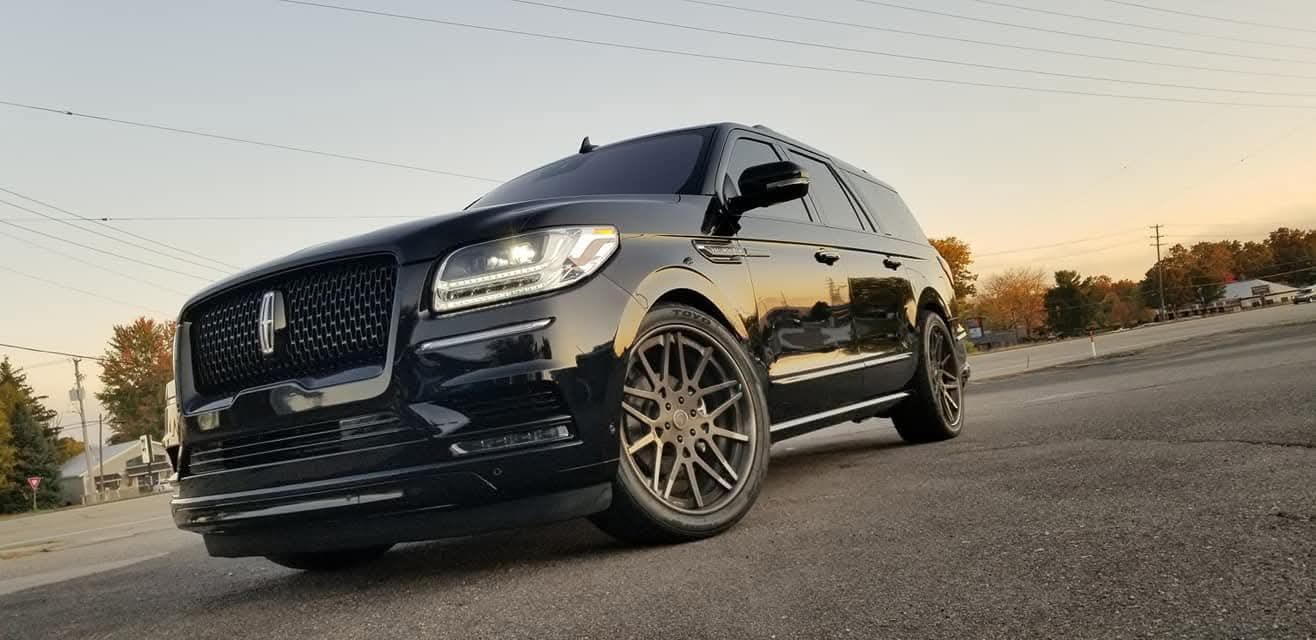 Black Lincoln Aviator SUV on a paved road with bronze-colored wheels, against an overcast sky.