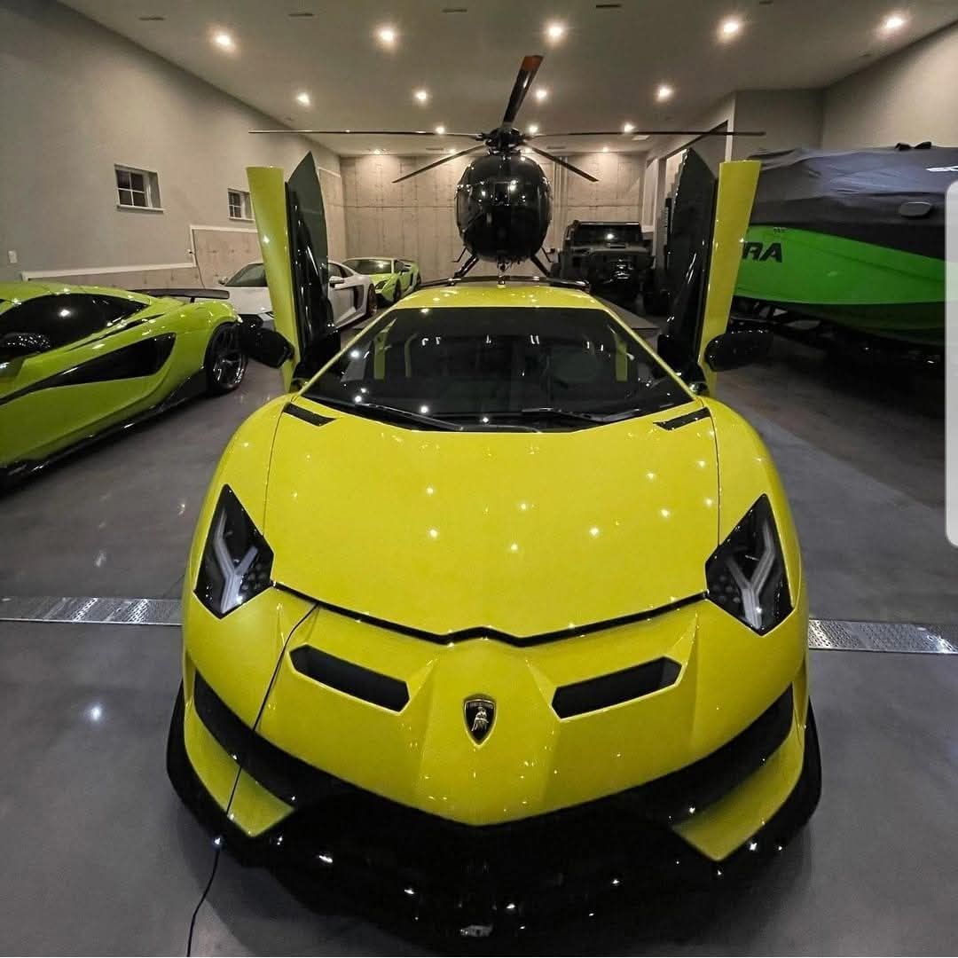 Yellow Lamborghini with doors open in a garage, helicopter in background. Other cars visible.