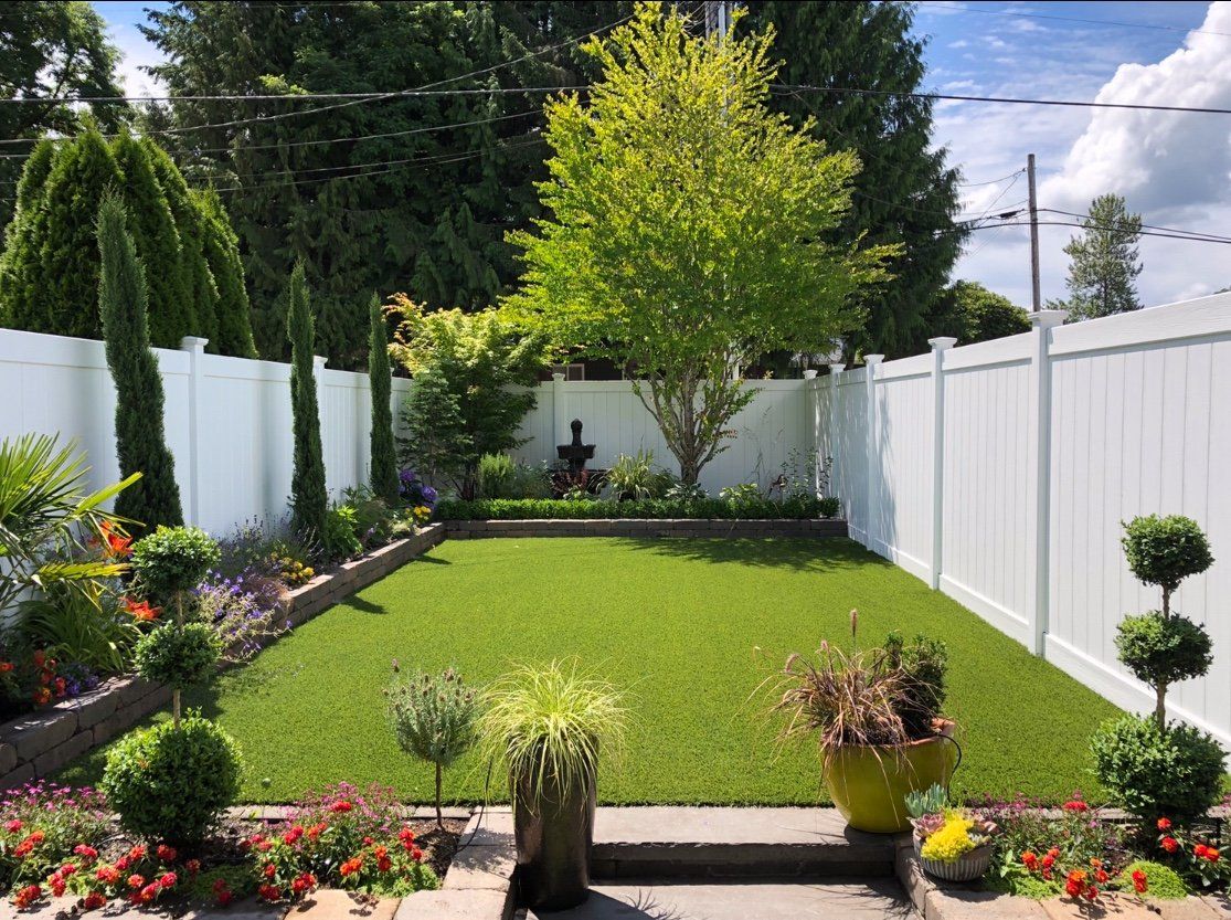 A backyard with a white fence and a lush green lawn.