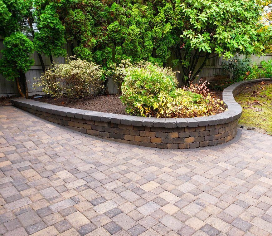 A brick patio with a curved wall and a tree in the background