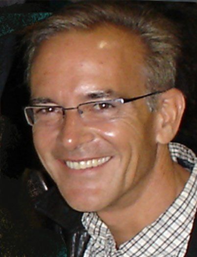 A man wearing glasses and a plaid shirt smiles for the camera