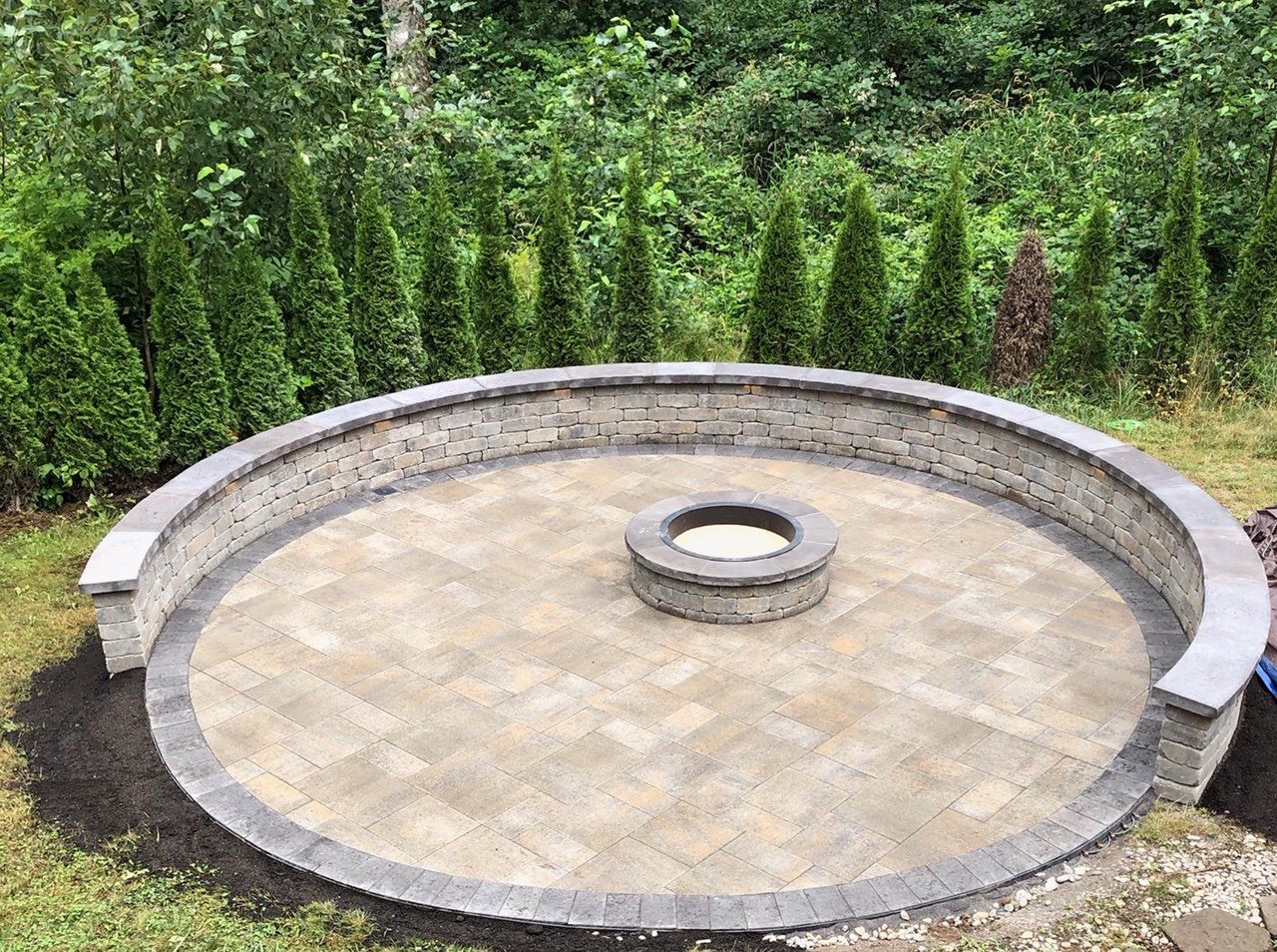 A circular patio with a fire pit in the middle surrounded by trees.