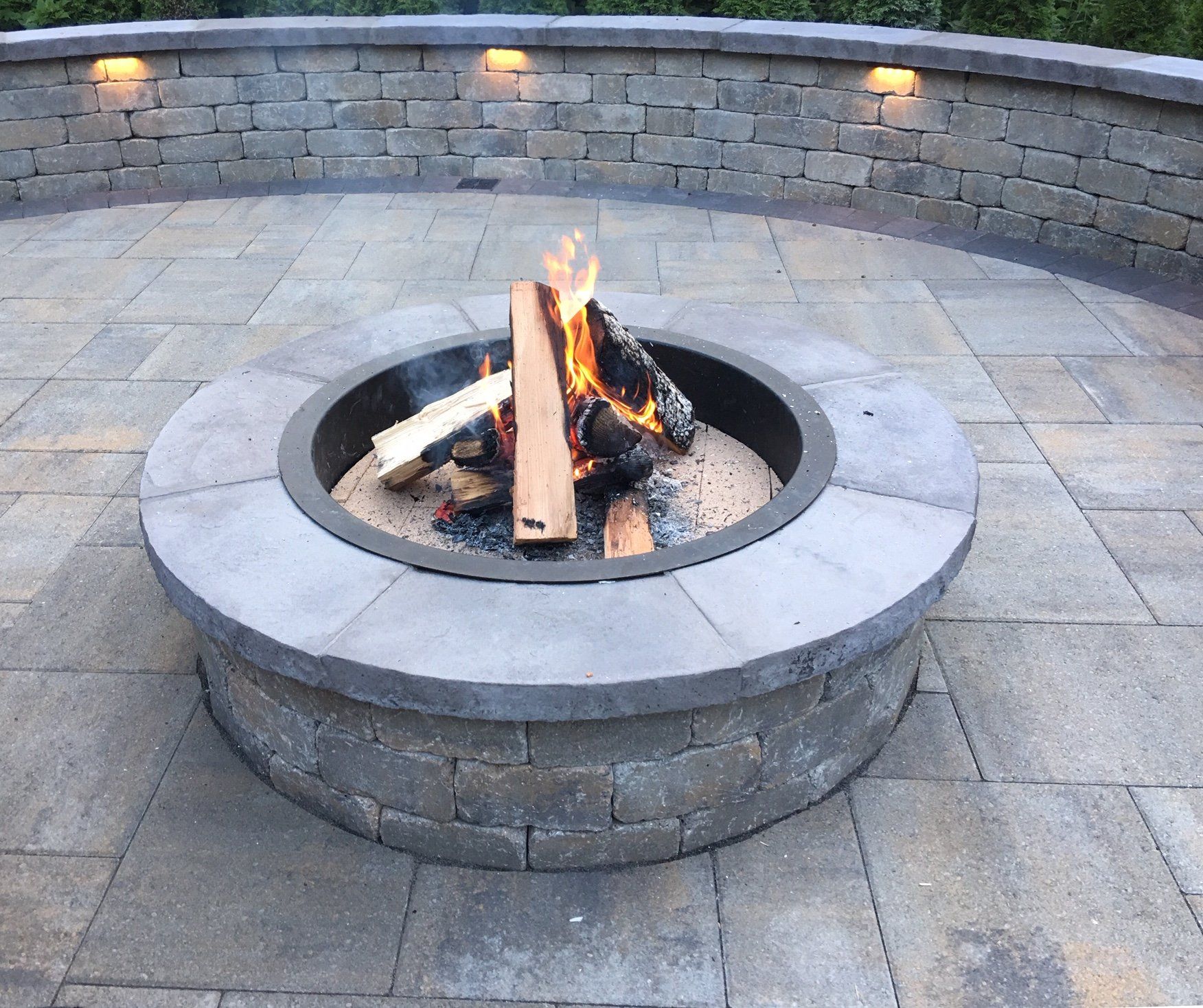 A fire pit on a patio with a brick wall behind it