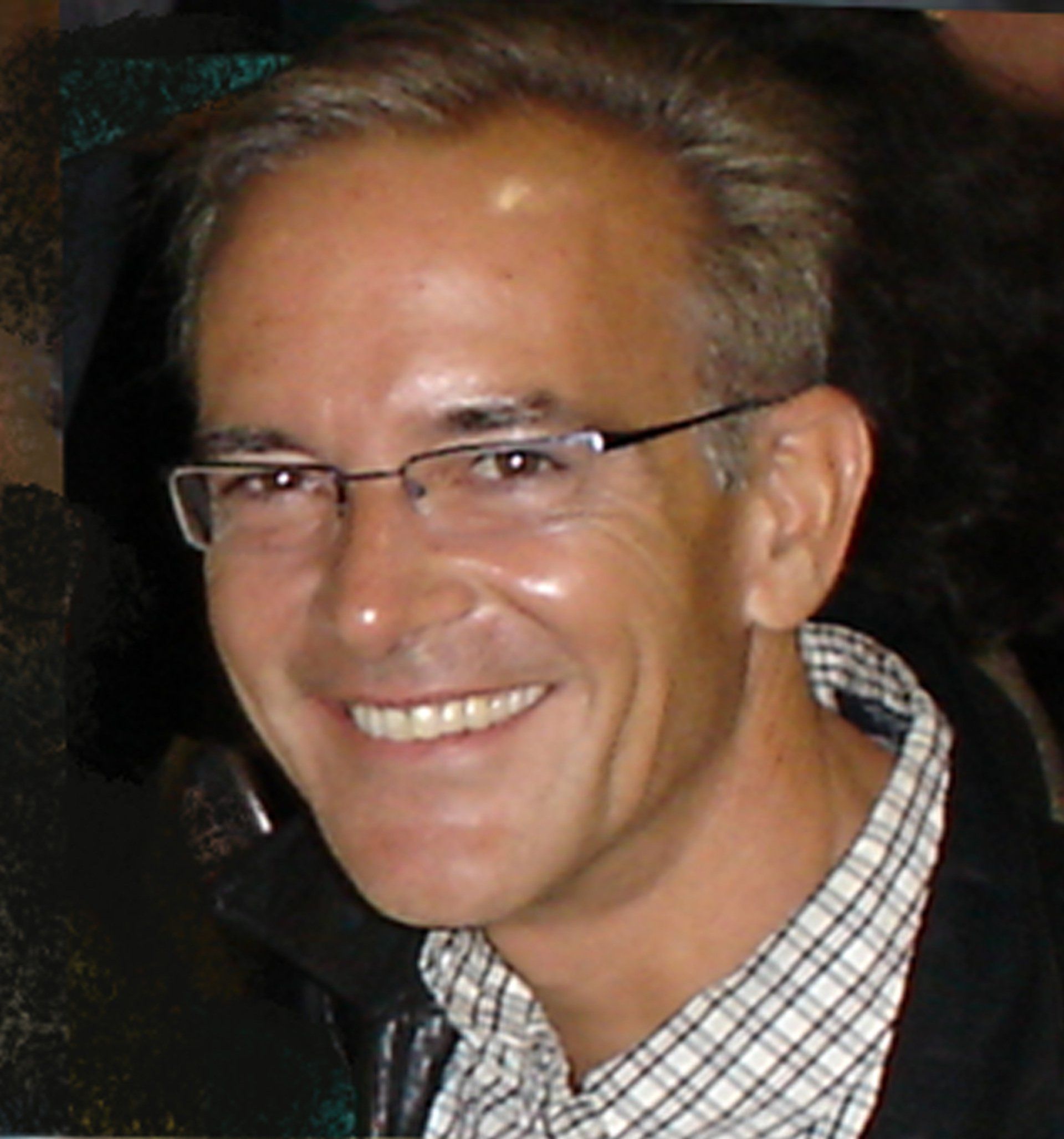 A man wearing glasses and a plaid shirt smiles for the camera