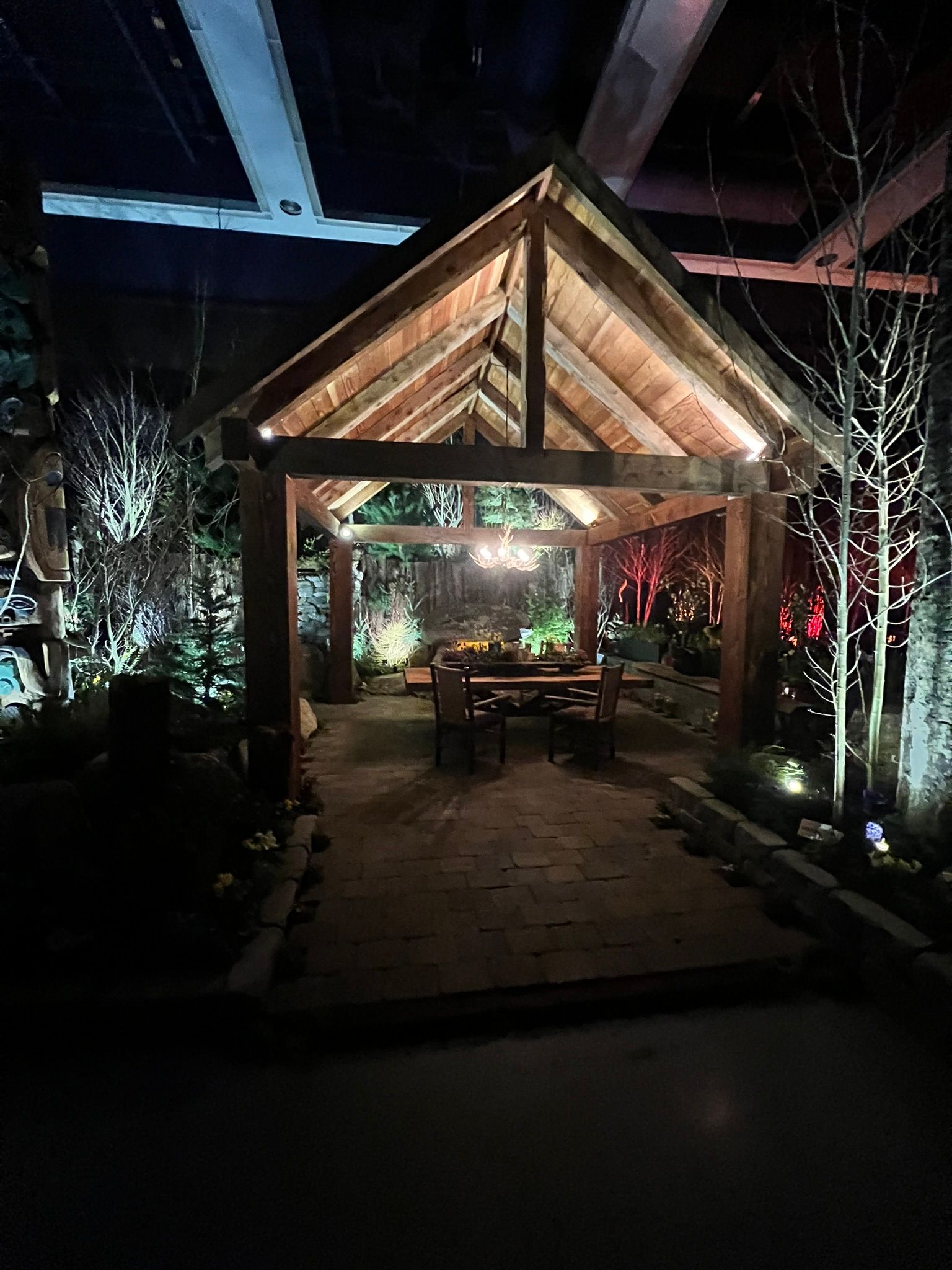 A wooden gazebo with a table and chairs underneath it is lit up at night.