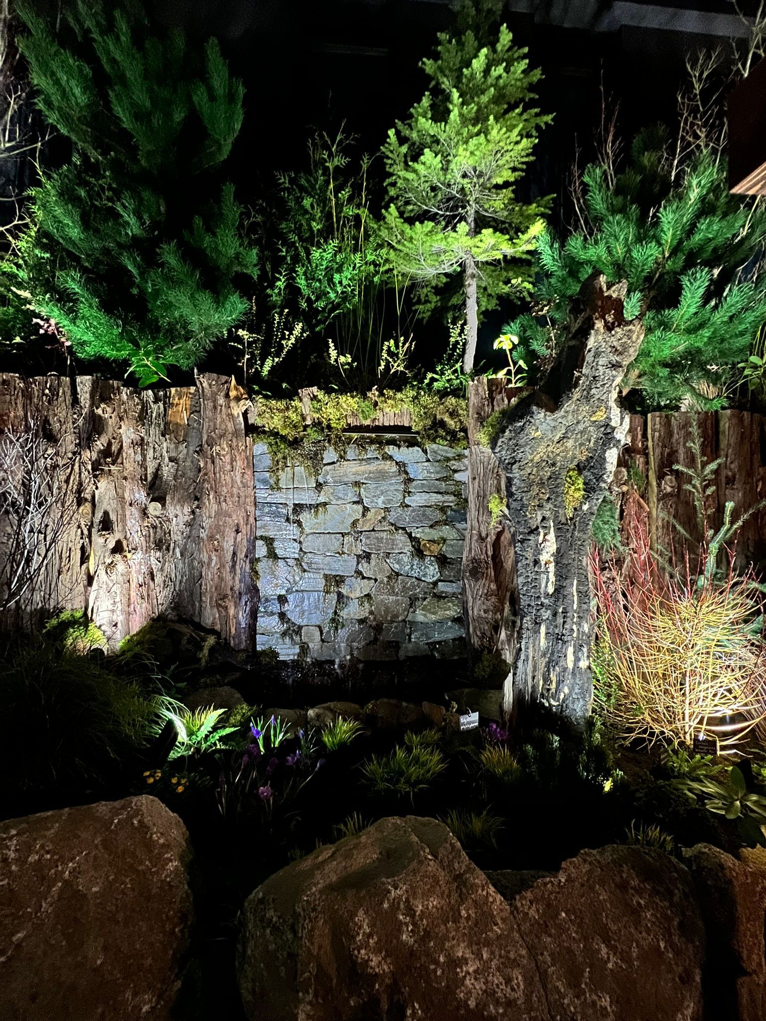 A stone wall is lit up at night with trees in the background.