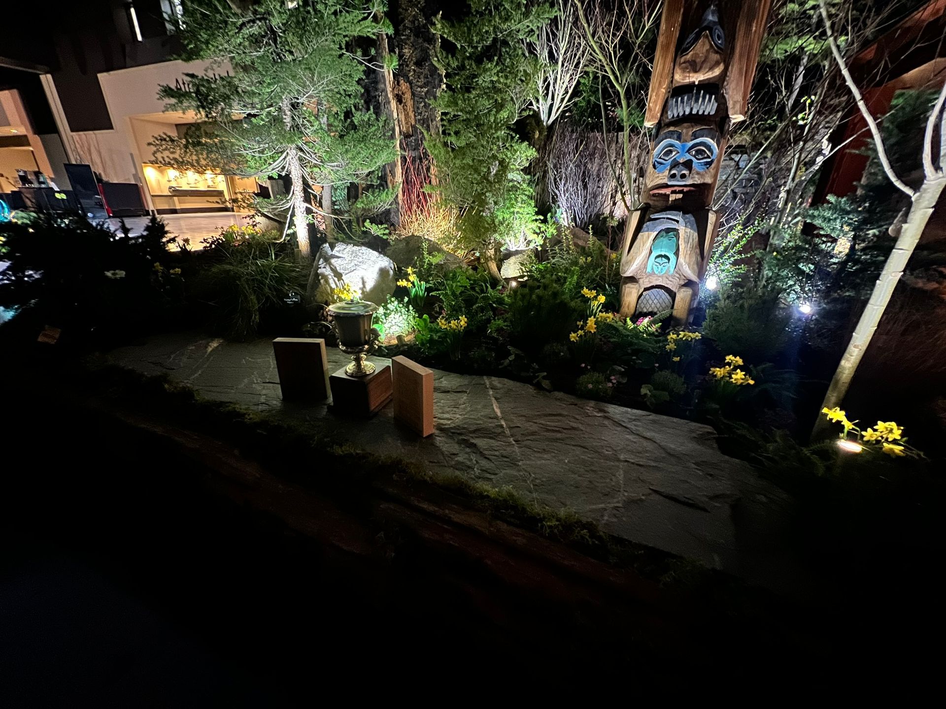 A garden with trees and flowers is lit up at night.