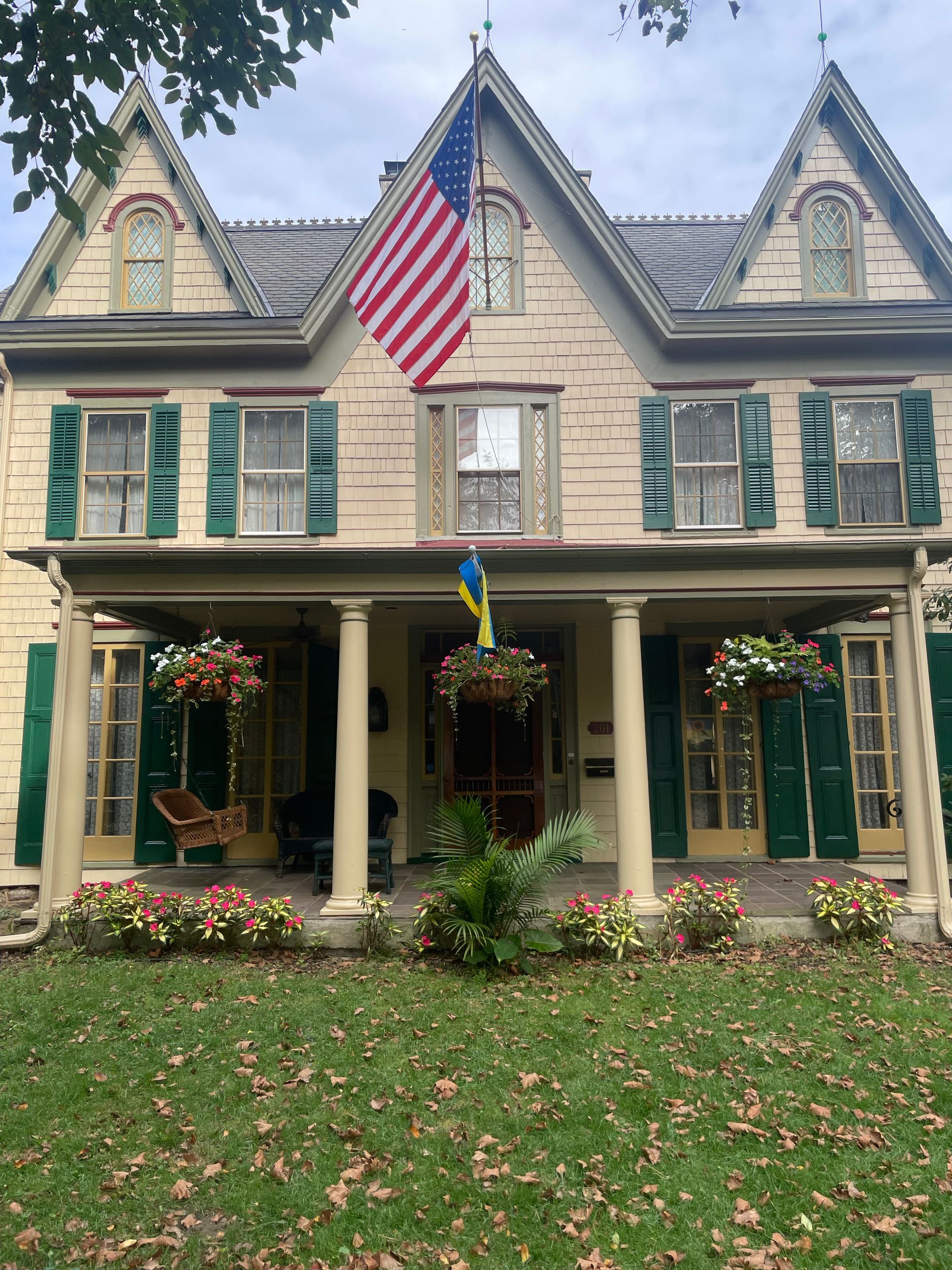 Two-story Victorian house with American flag, Ukrainian flag, green shutters, porch with flowers.