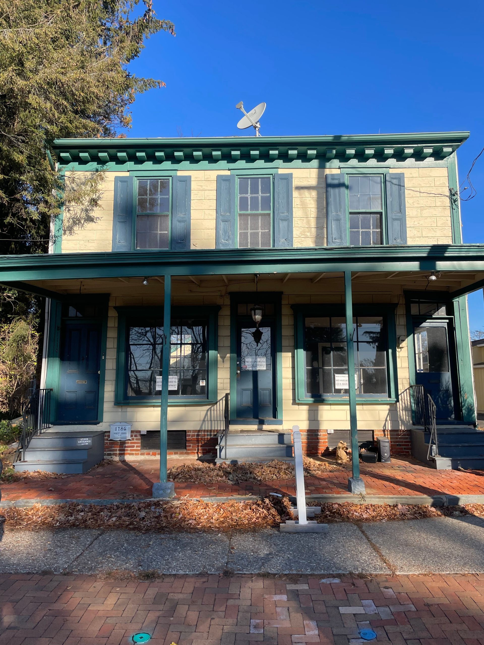 Two-story yellow house with green trim and porch. Blue shutters and a satellite dish on the roof.
