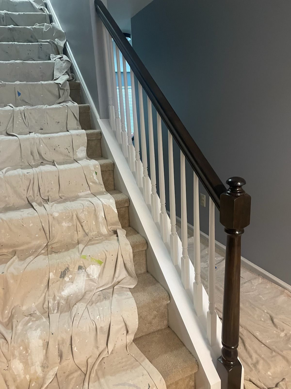 Staircase with white balusters, dark brown handrail and newel post, and steps covered in protective material.