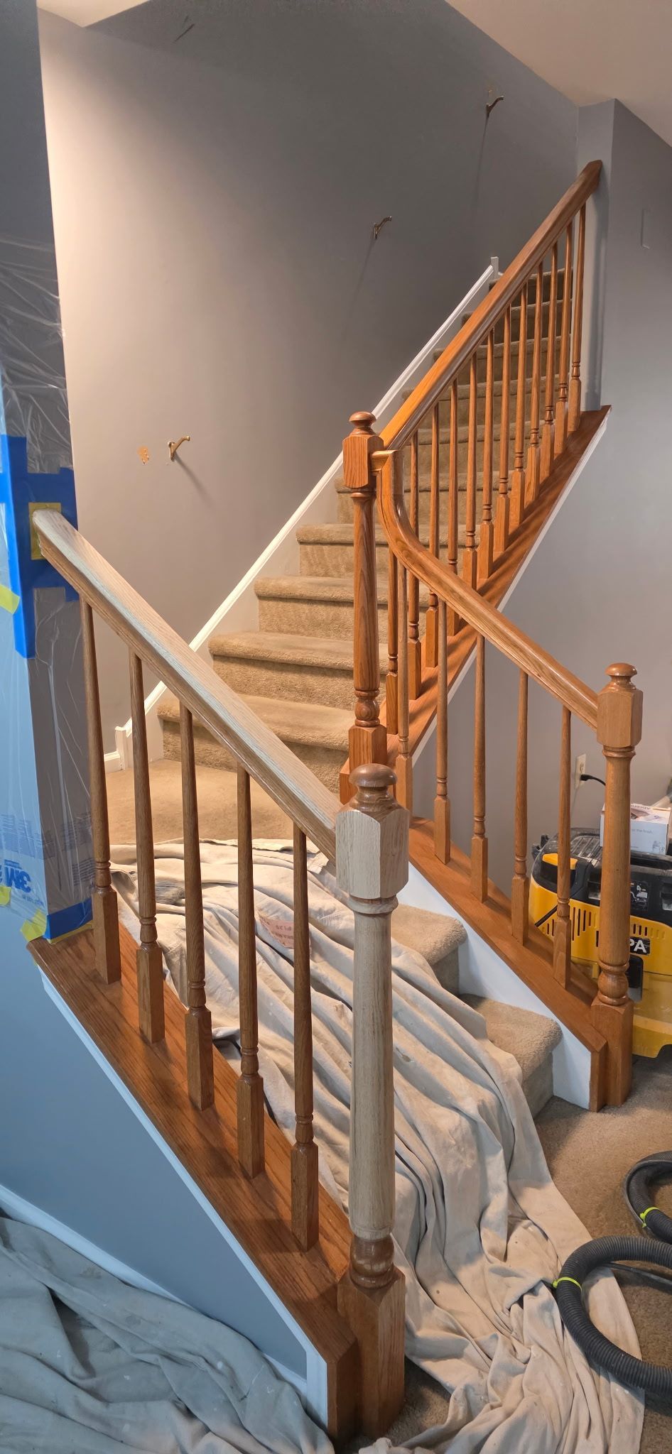 Staircase with wooden railings, some painted, under construction. Stairs have carpet. Light gray walls.