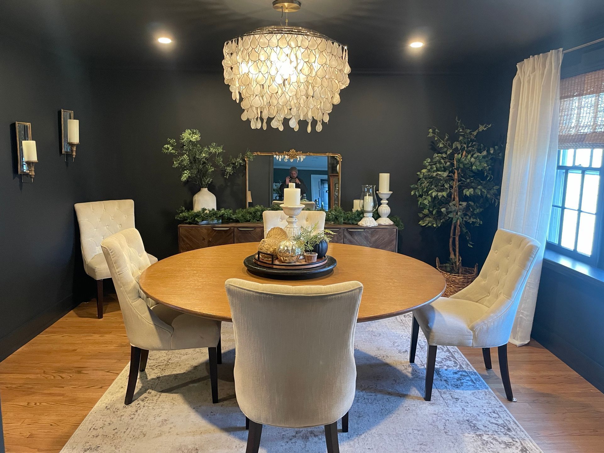Elegant dining room with dark walls, round wood table, chandelier, and upholstered chairs.