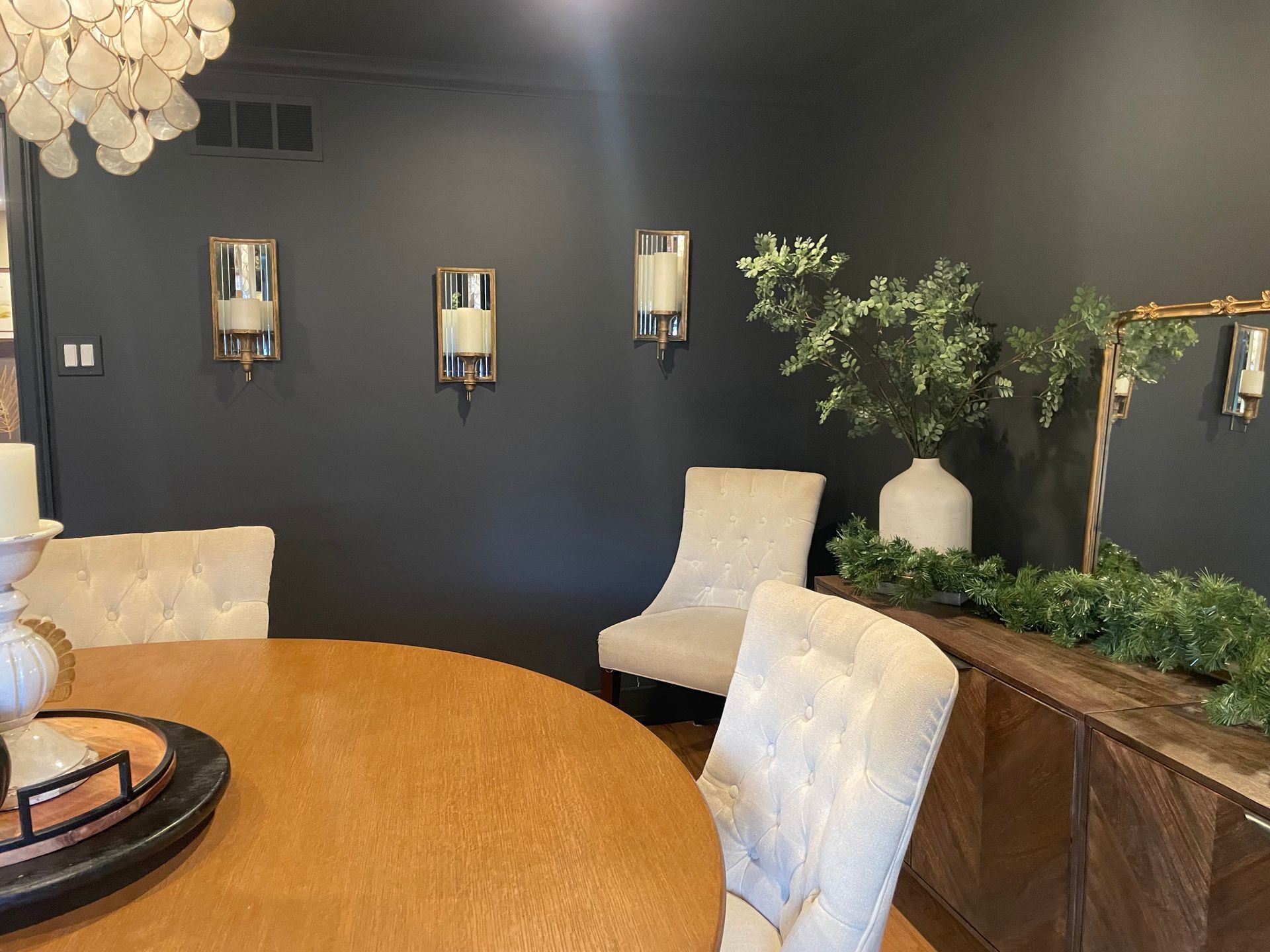 Formal dining room with dark gray walls, gold sconces, wooden table, and tufted chairs.