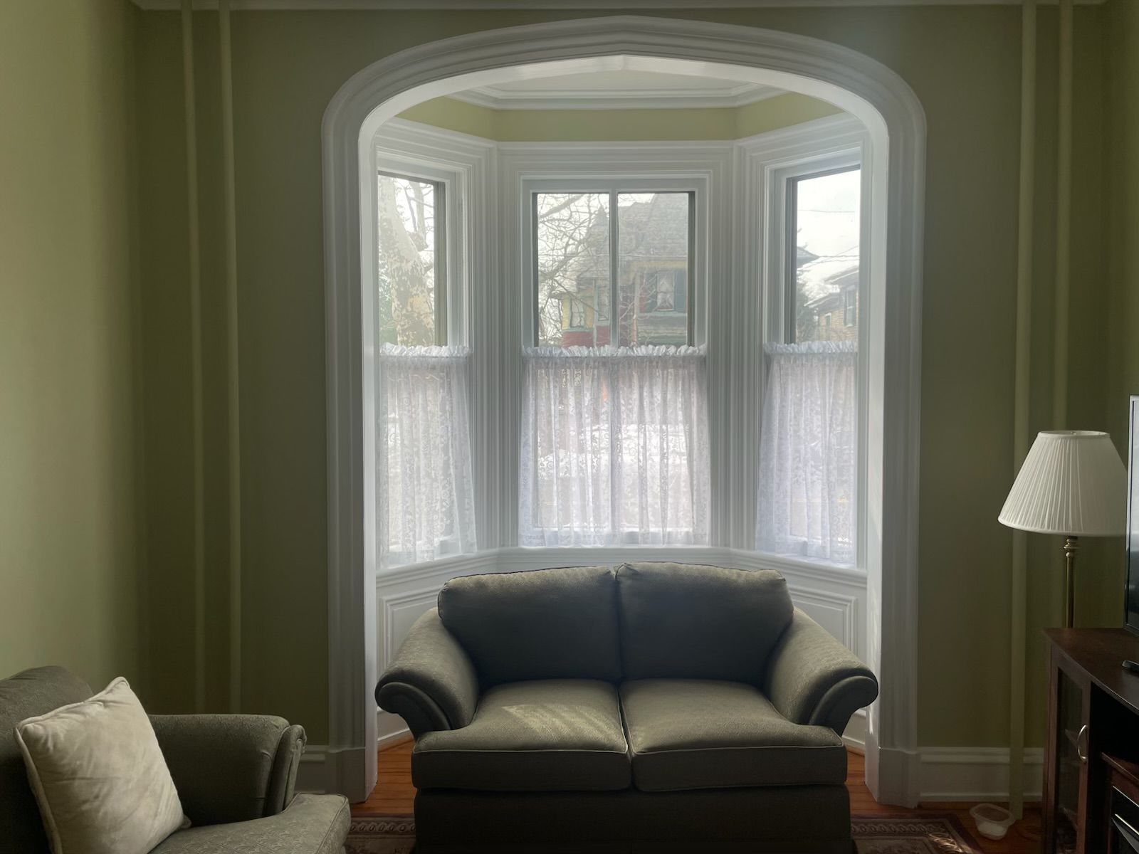 Green room with a bay window, armchair, and sheer curtains.