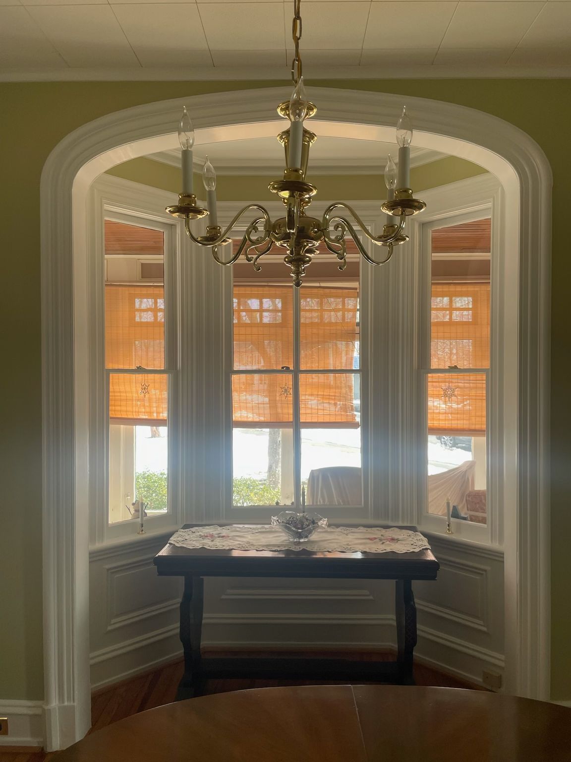 A dining area with a decorative chandelier over a table set in a window alcove with woven blinds.
