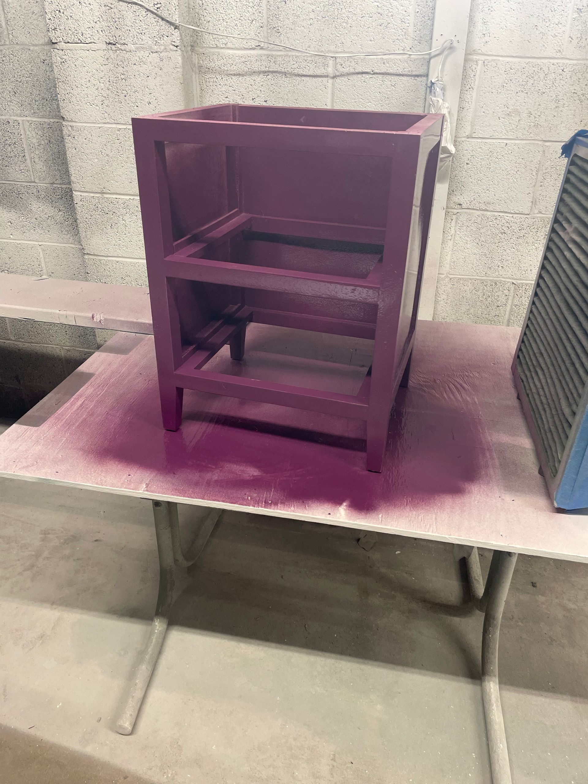 Purple painted wooden cabinet on a folding table, spray paint residue visible.