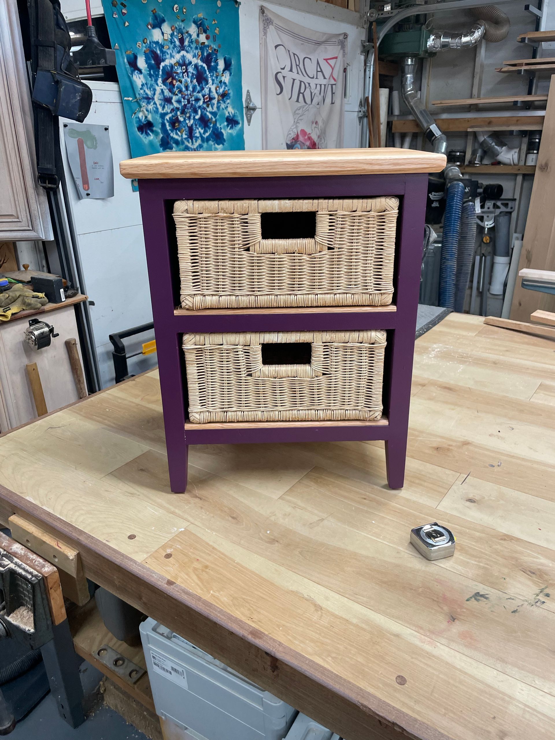 Purple and wood cabinet with two wicker baskets on a wooden workbench.