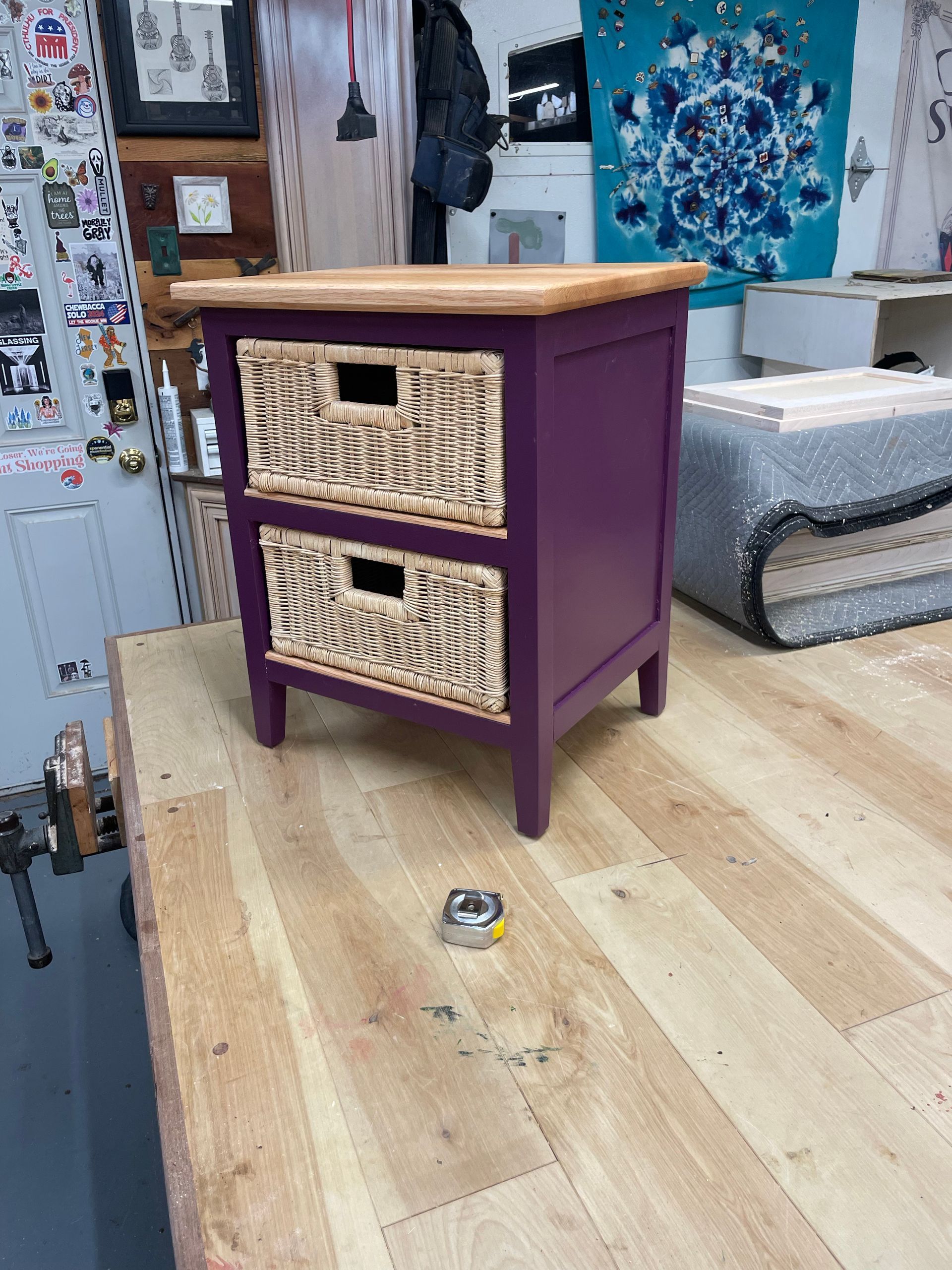 Purple nightstand with wicker drawers on a wooden tabletop, tape measure in front.