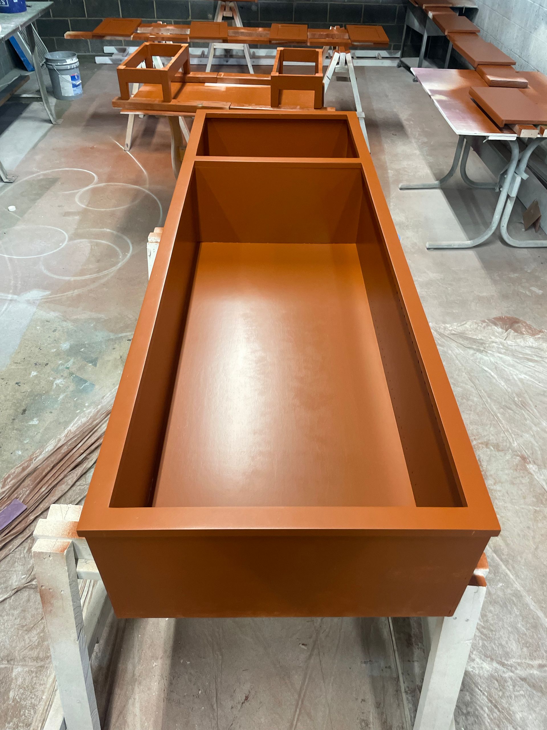 Brown painted rectangular planter box on sawhorse, another in the background. Workshop setting.