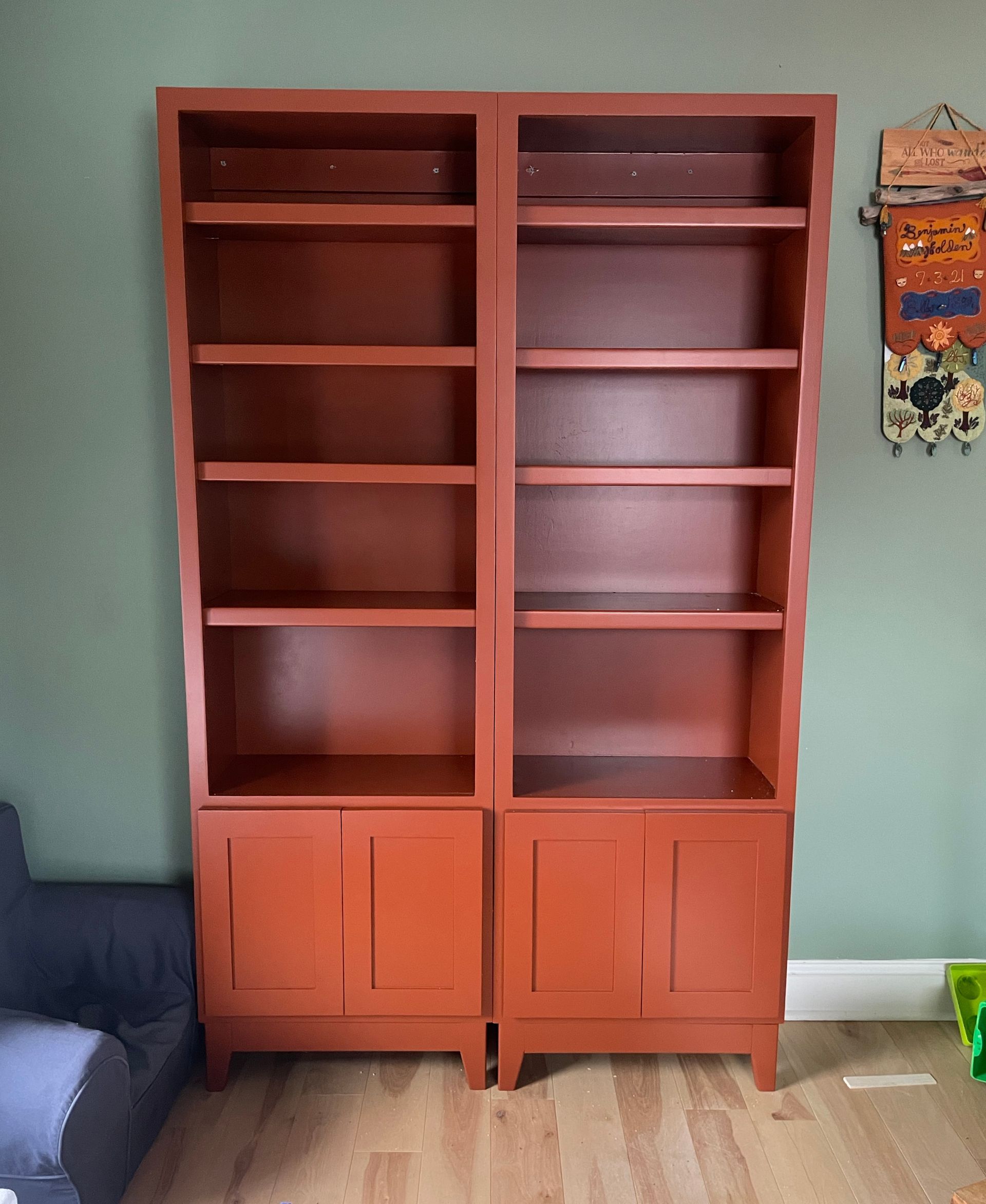 Two tall, reddish-brown bookshelves with open shelving above and cabinet doors below, against a green wall.