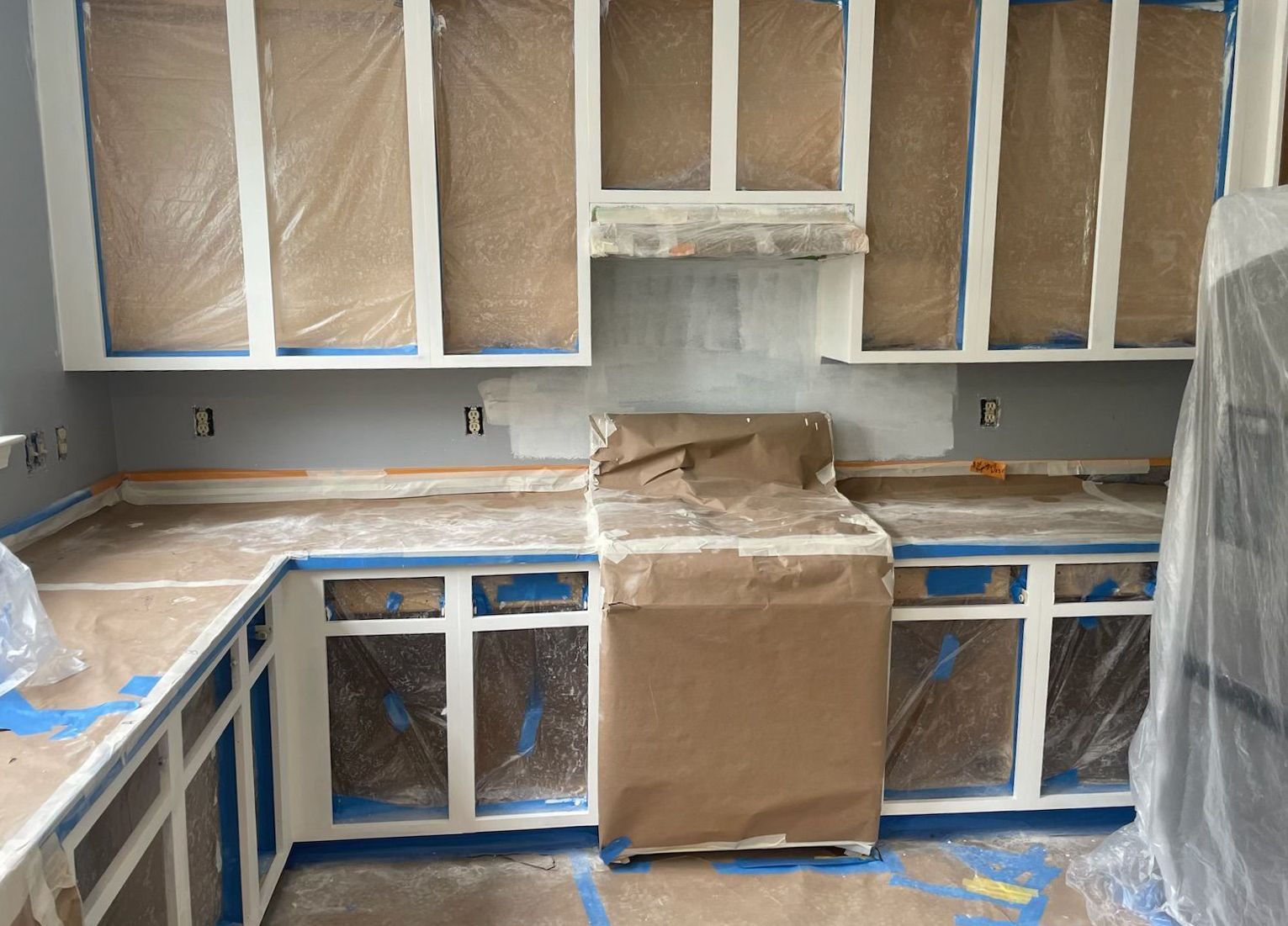 Kitchen cabinets being painted white; countertops and appliances covered for protection.