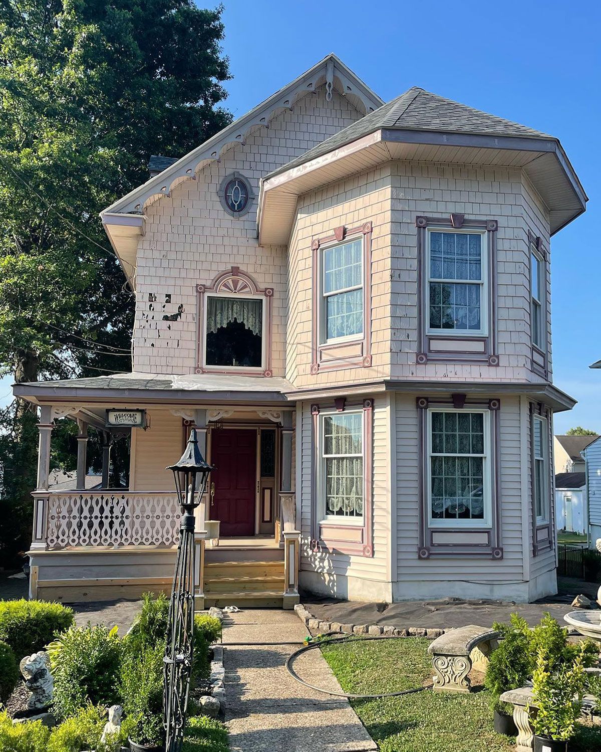 Two-story Victorian house, light pink exterior, porch with ornate railing, front door, small garden.