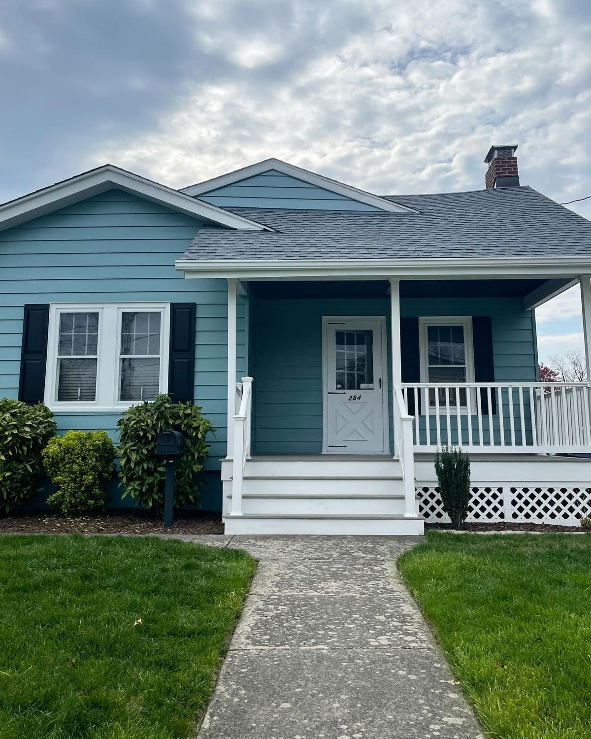 Blue house with white trim, porch, and a walkway leading to the front door.