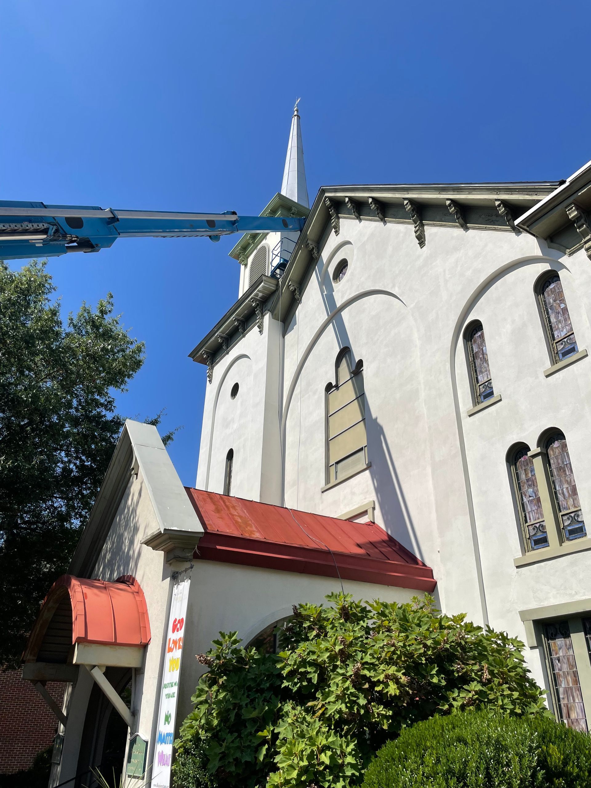 Church exterior with blue lift, white walls, and red roof under a clear, blue sky.