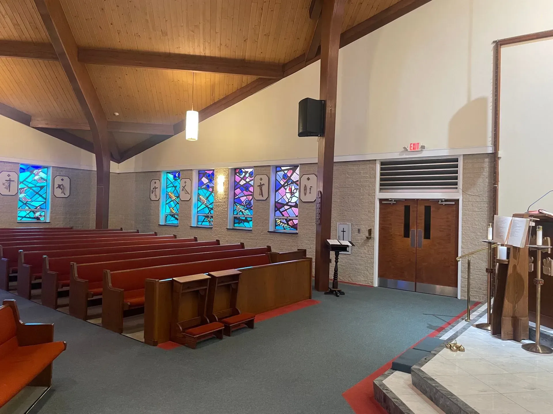 Interior church with wooden beams, stained glass windows, rows of pews, and altar.