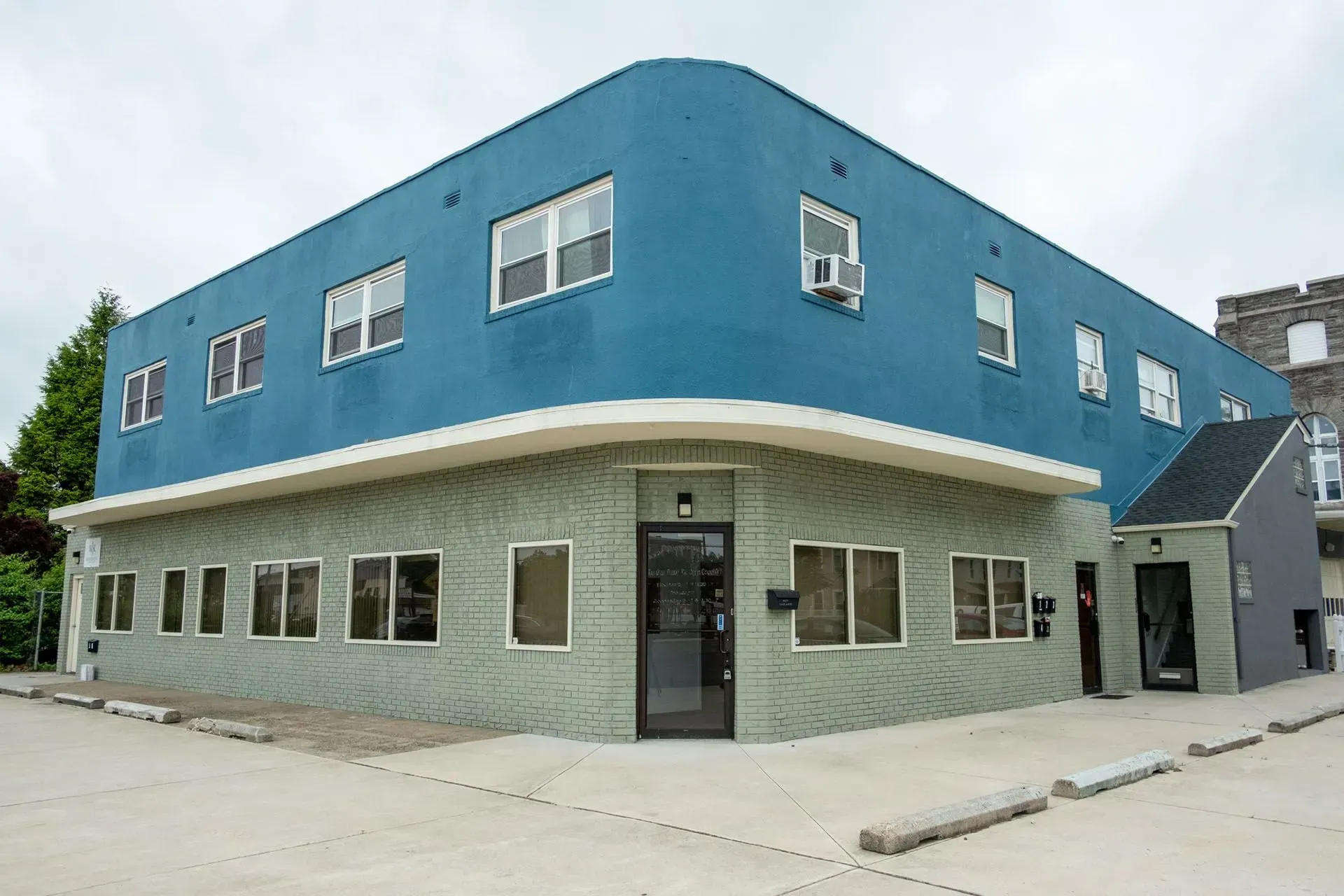 Blue and green two-story building with rounded corner, windows, and black door.