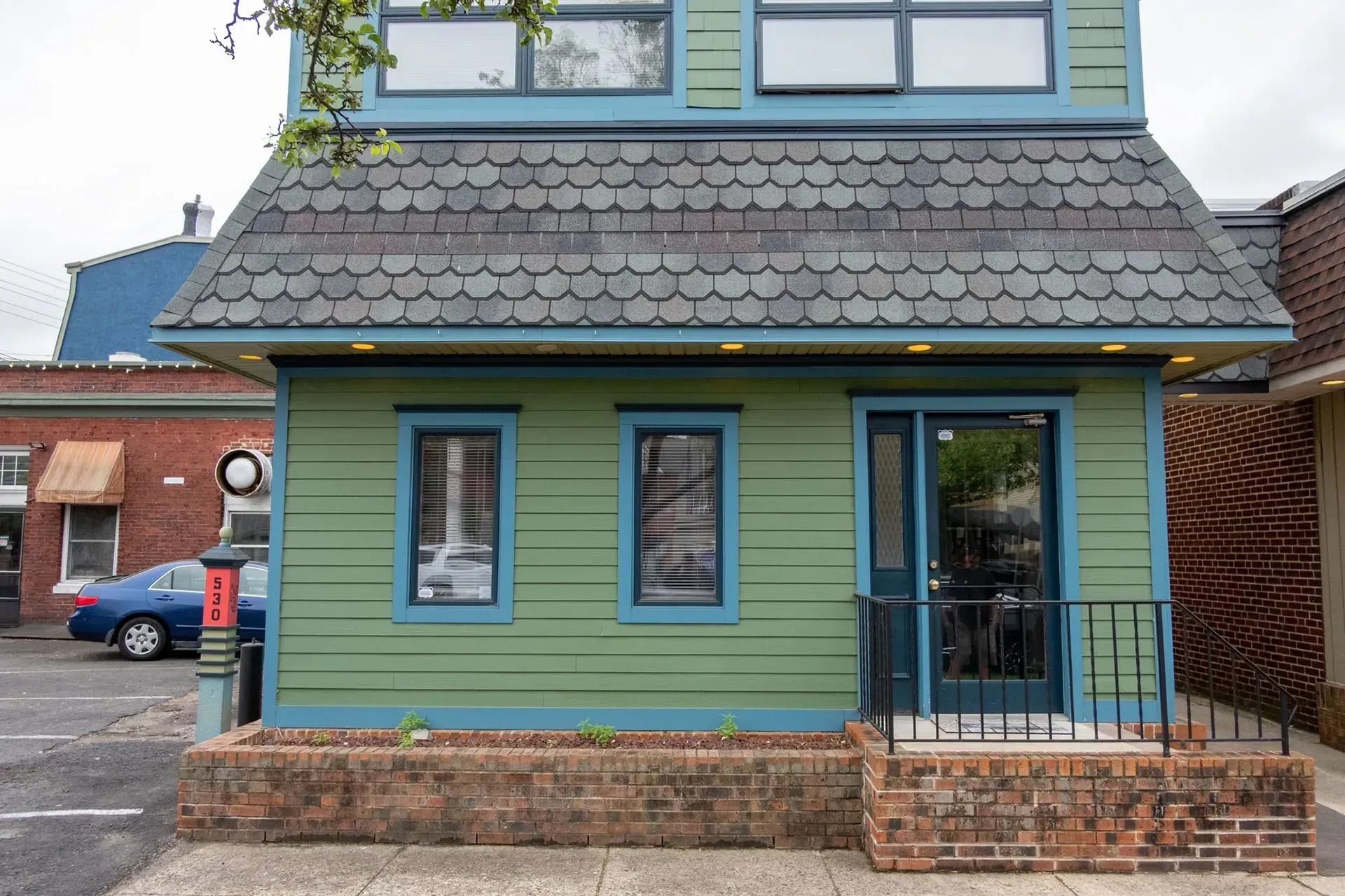 Green building with blue trim, windows, and black door, on brick foundation.