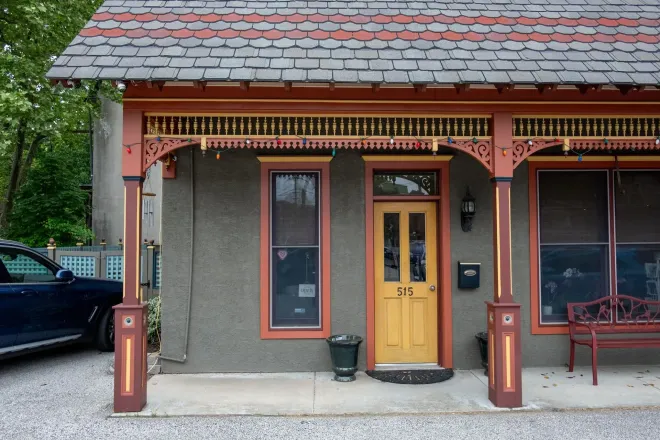 Gray building with a decorative brown porch, yellow door, and windows. A car is parked on the left.