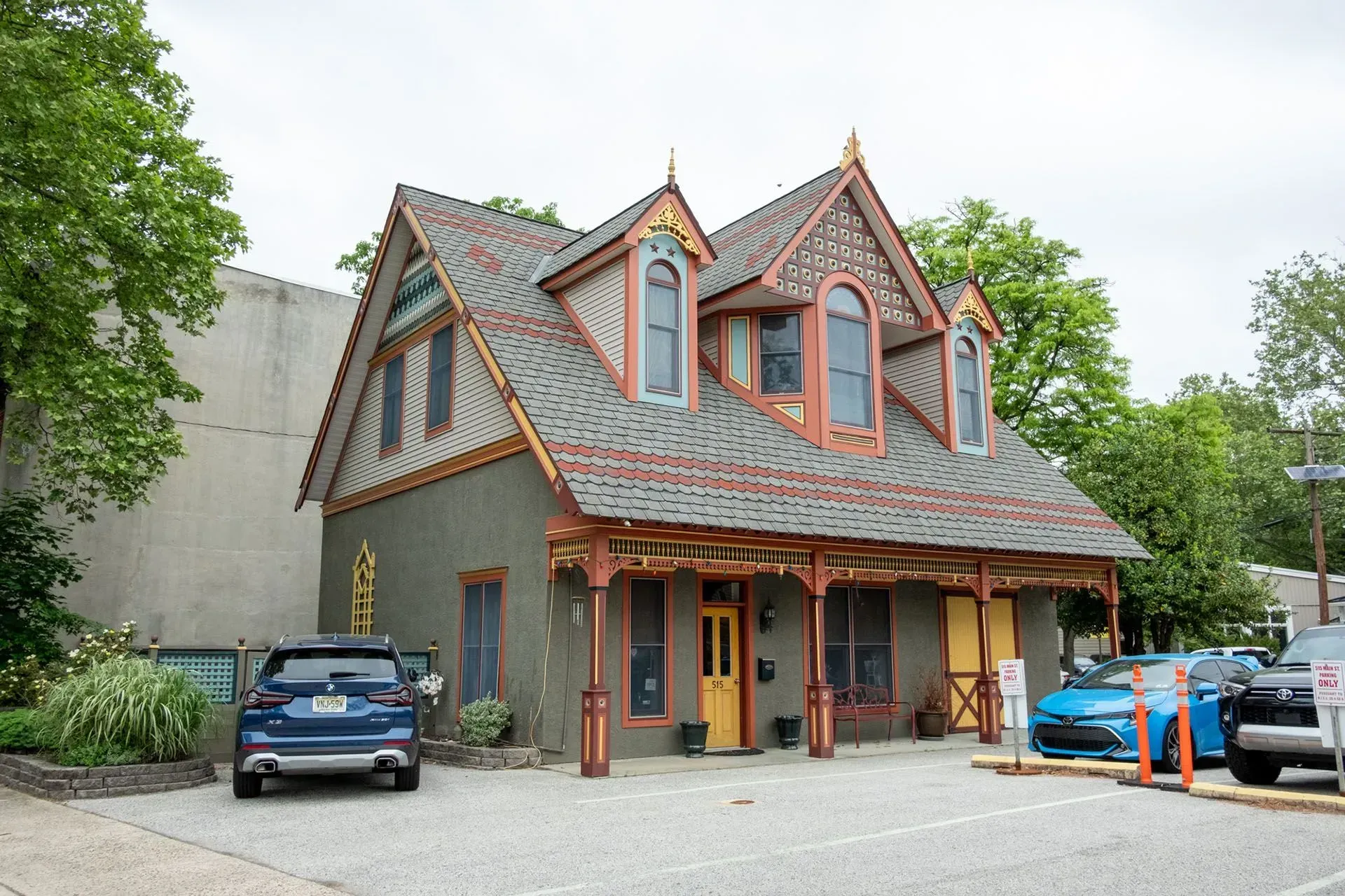 Ornate gray, brown and orange building with a covered porch and parked cars in front.