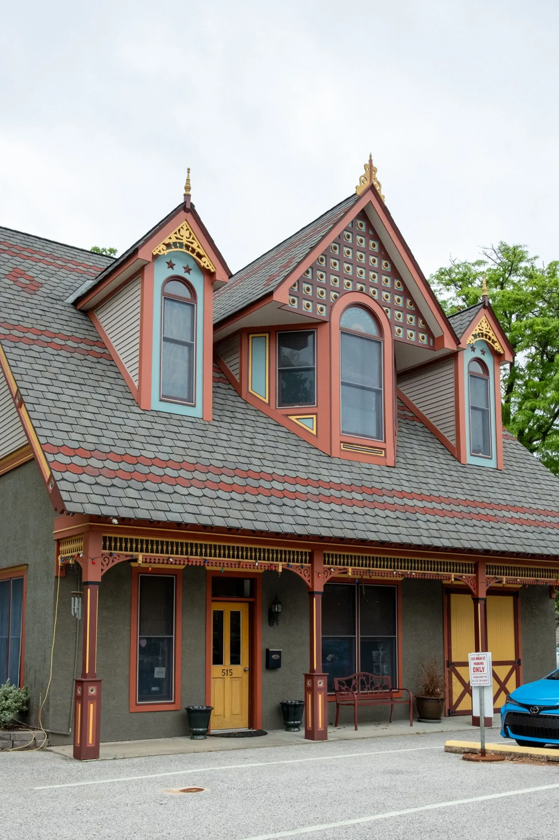 Ornate, Victorian-style building with grey roof and dark red trim. Three dormers with arched windows. Yellow door.