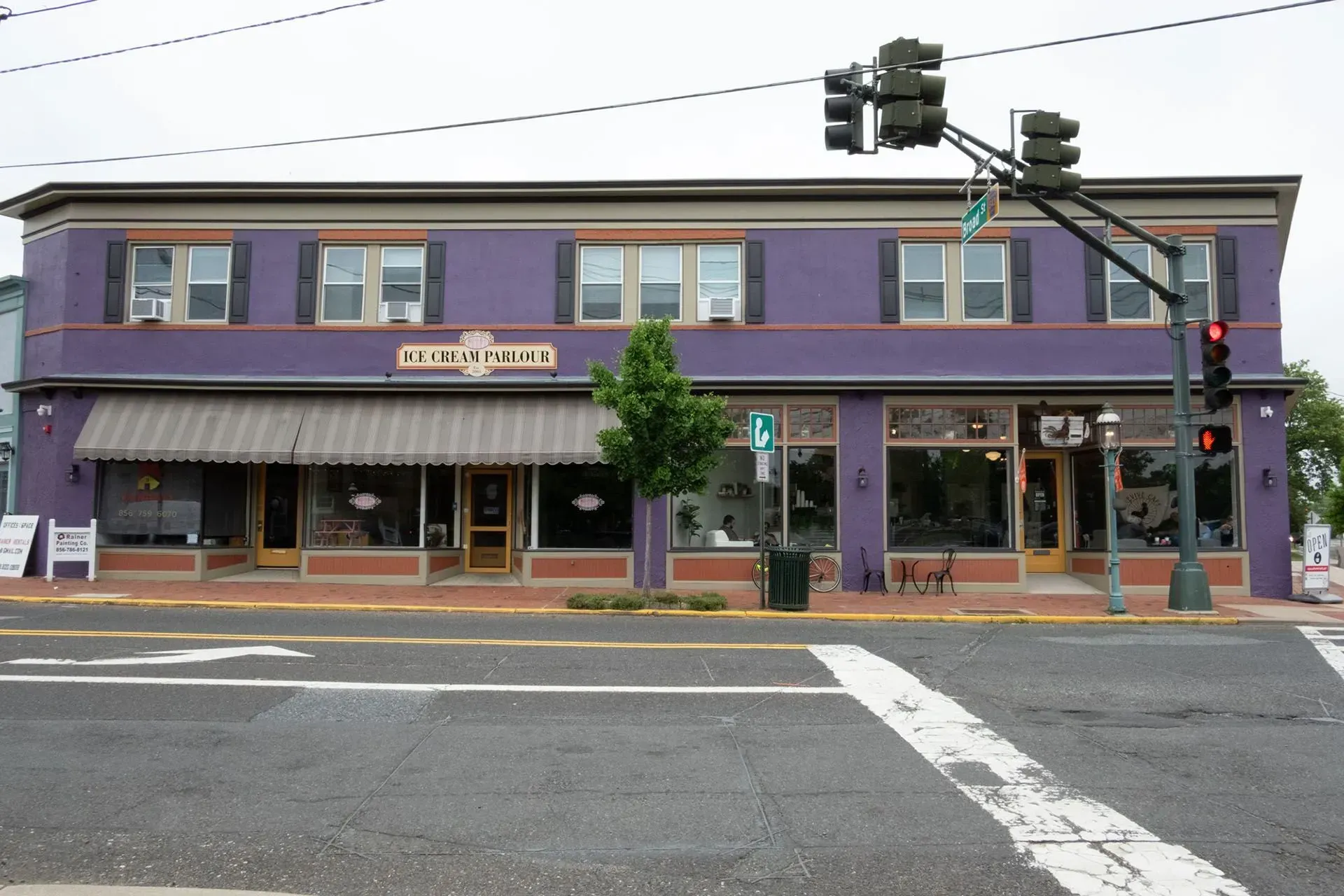 Purple two-story building with storefronts. Street in foreground, traffic light overhead.