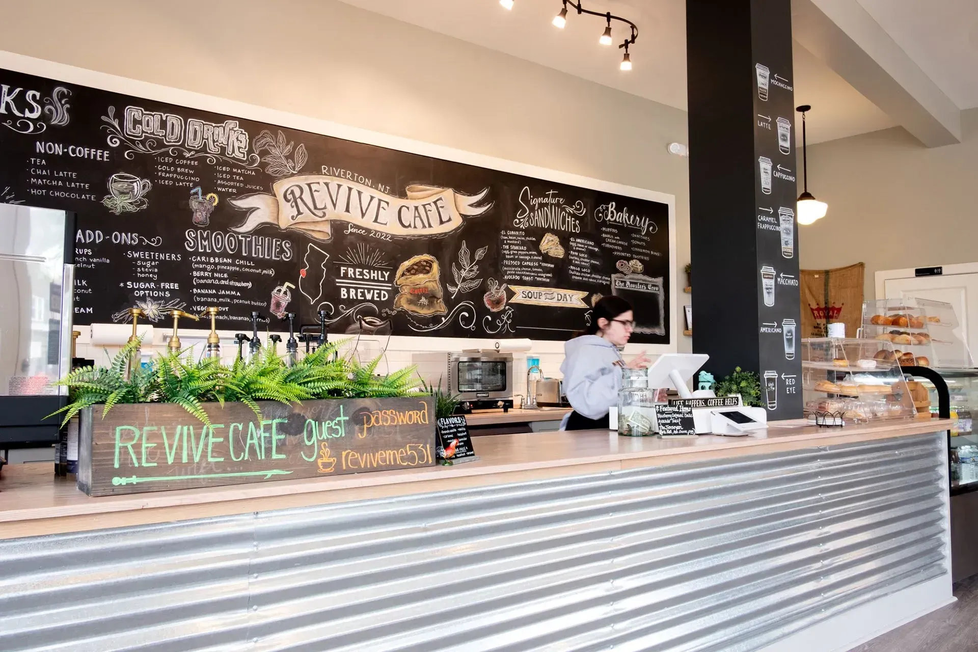 A barista at the counter of Revive Cafe, working behind a counter with a chalkboard menu.