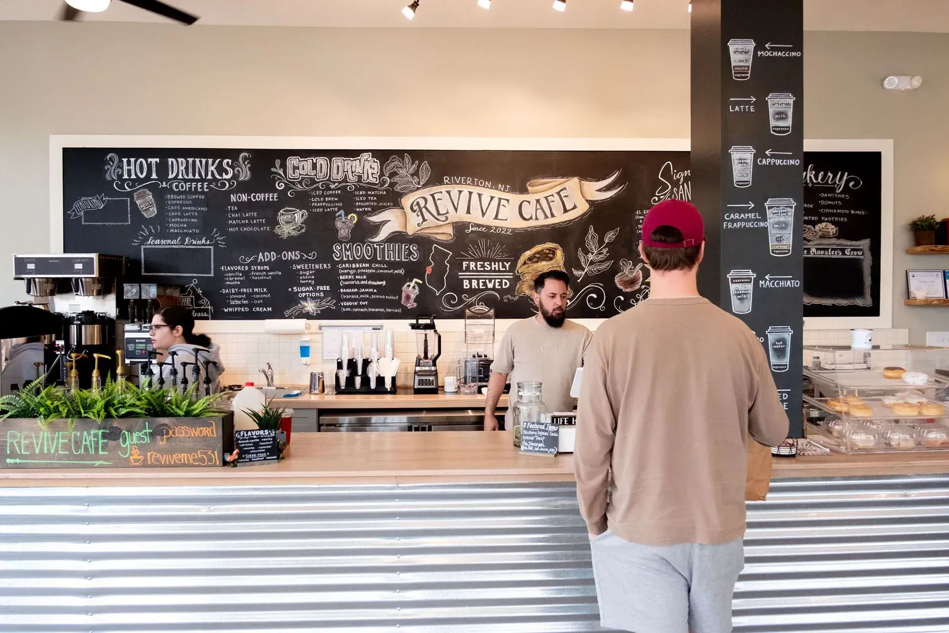 Customer at Revive Cafe counter ordering drinks. Cafe has chalkboard menu.