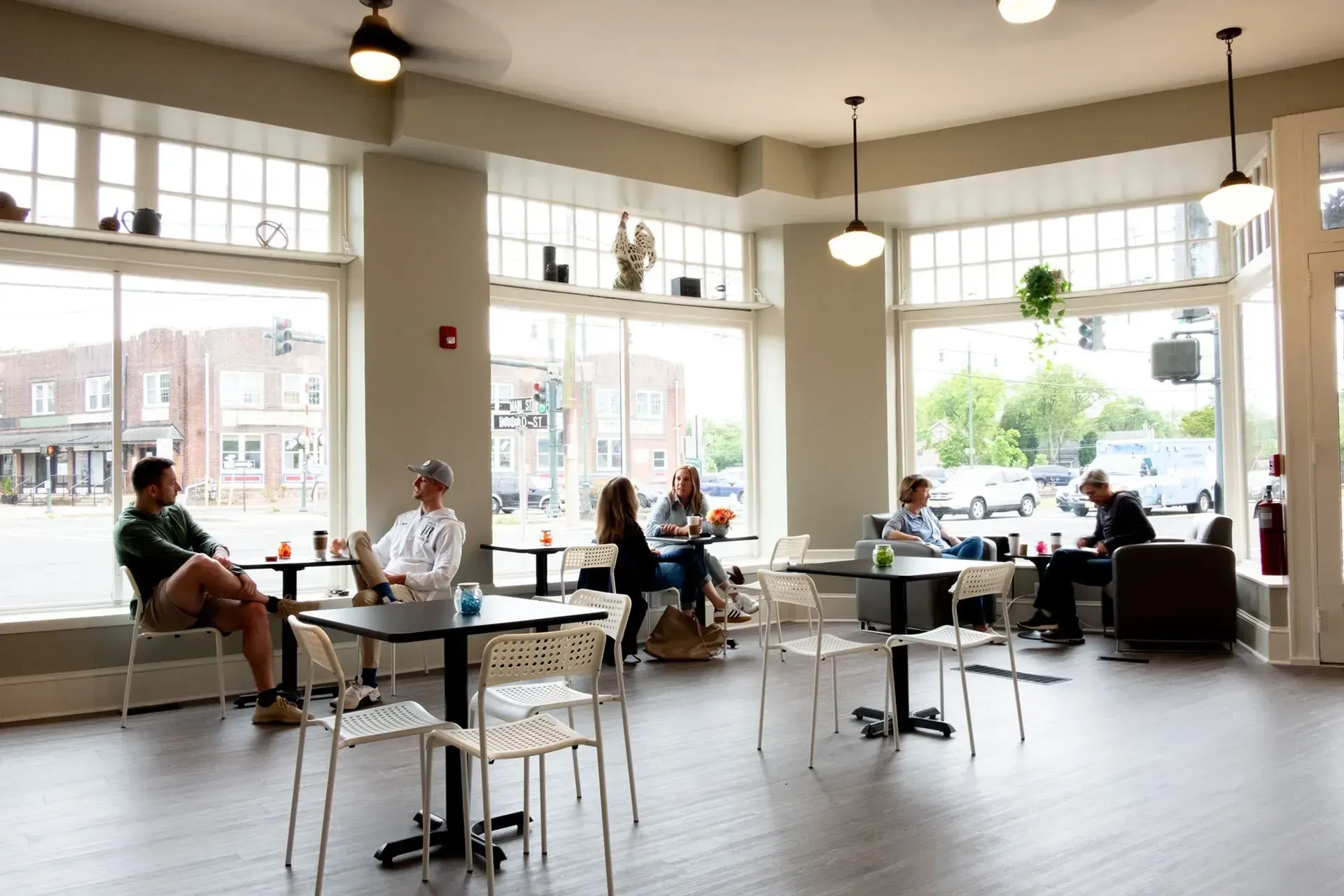 Coffee shop interior with several people seated at tables near large windows; natural light.
