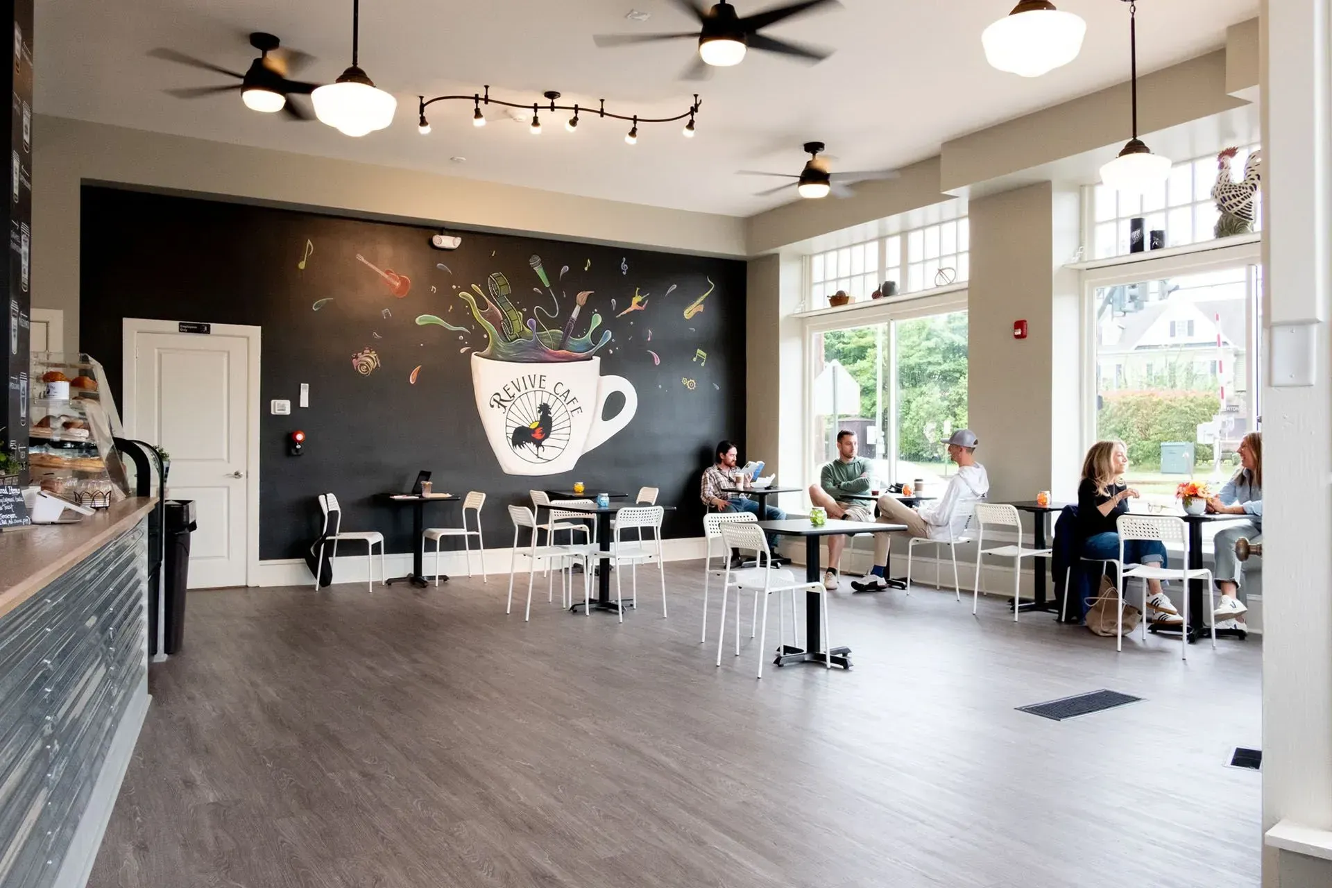 Coffee shop interior with customers, chalkboard art, tables, chairs, and ceiling fans.