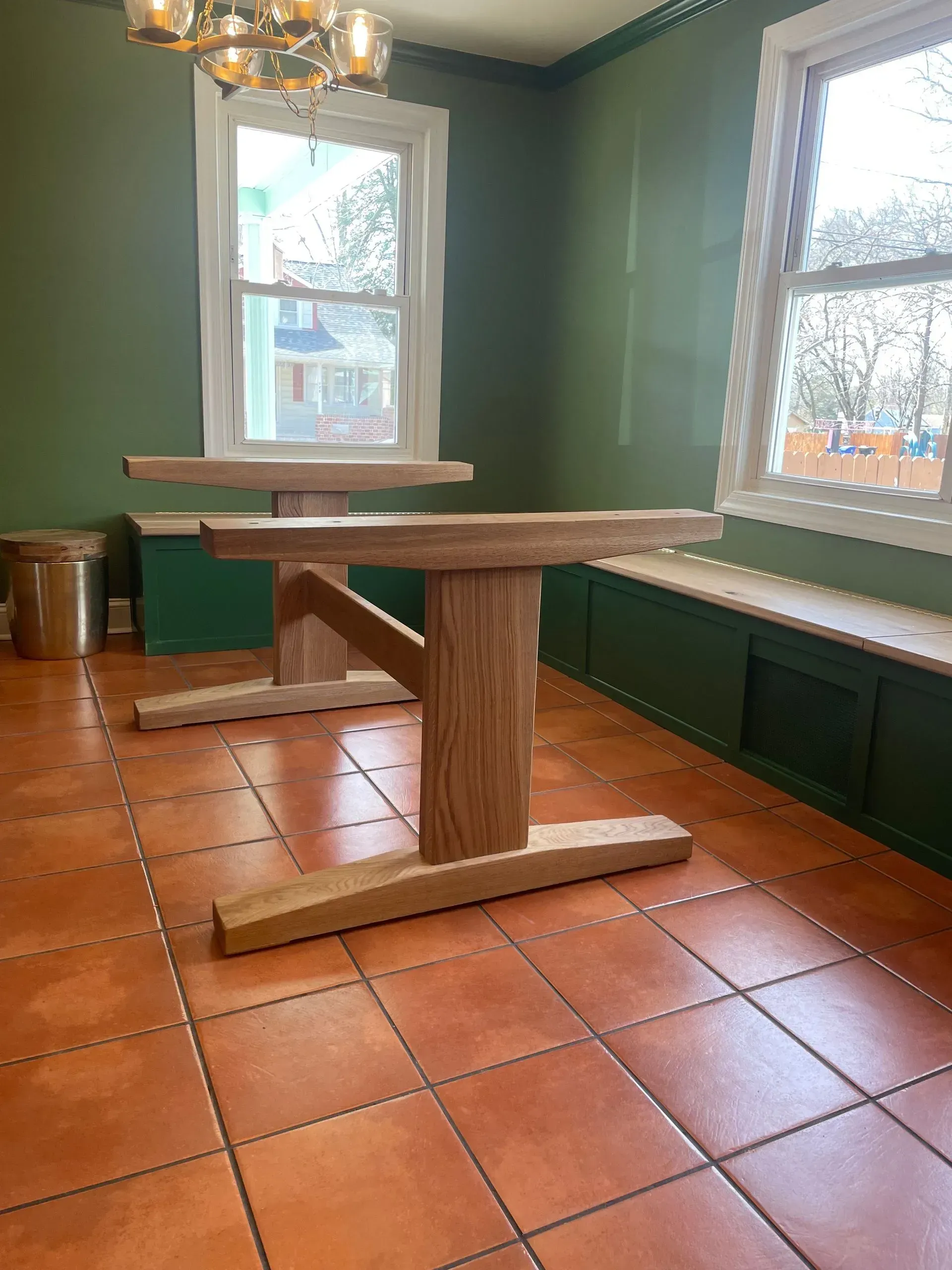 Two wooden tables on orange tiled floor, beside green built-in seating under windows.