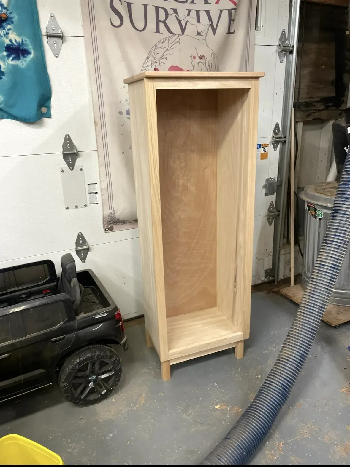 A tall, unfinished wooden cabinet in a workshop, with a hollow interior and a rectangular frame.