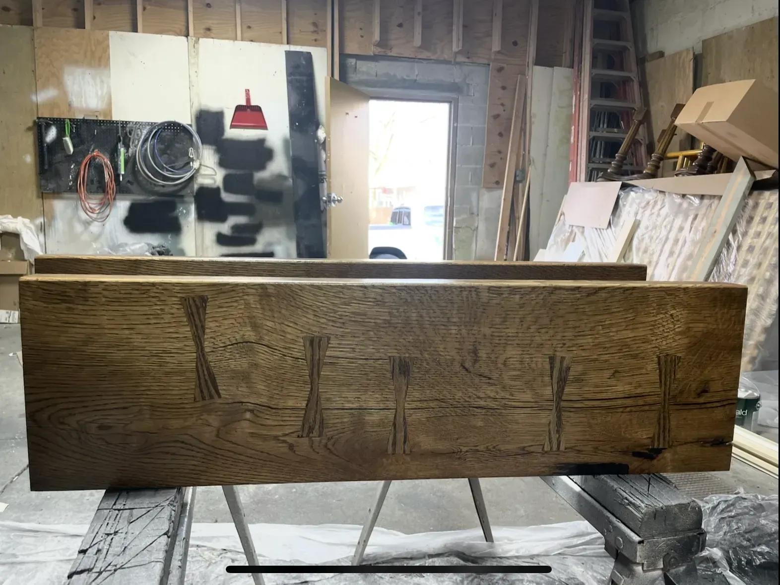 Wooden beam with decorative butterfly joints on sawhorses in a workshop setting.