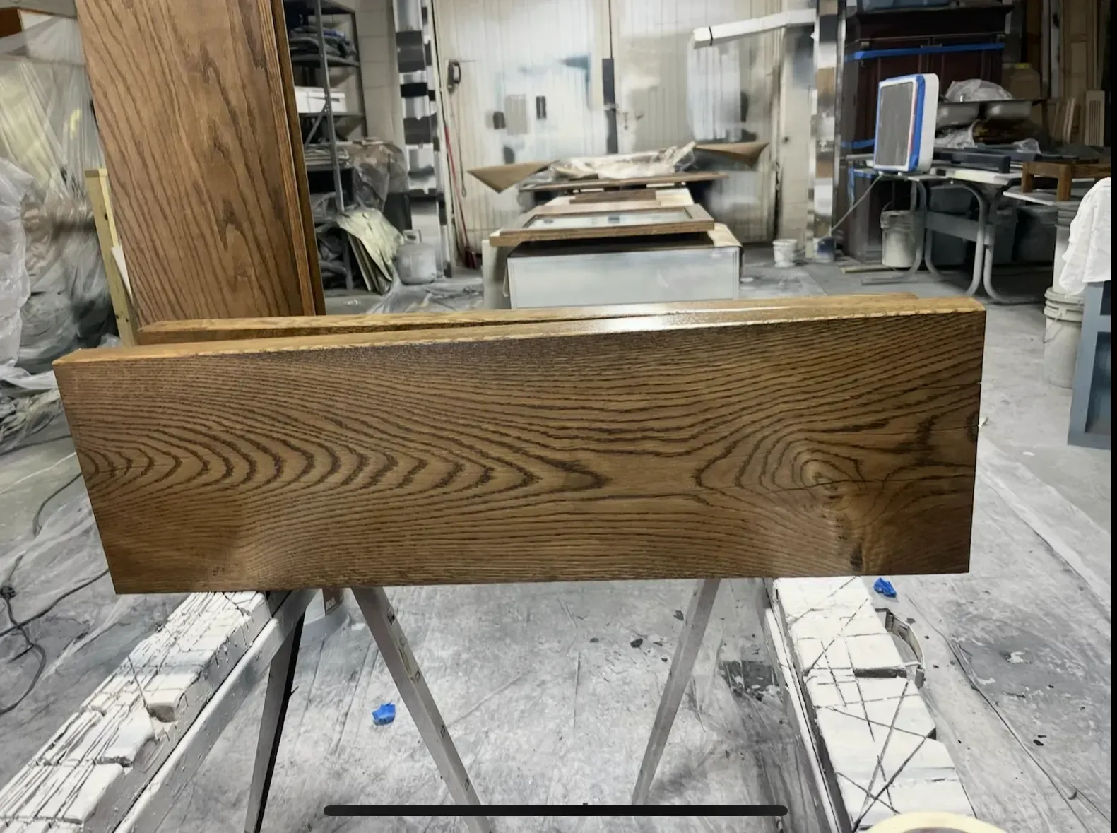 Wooden plank on a sawhorse in a workshop; it has a stained, natural finish.