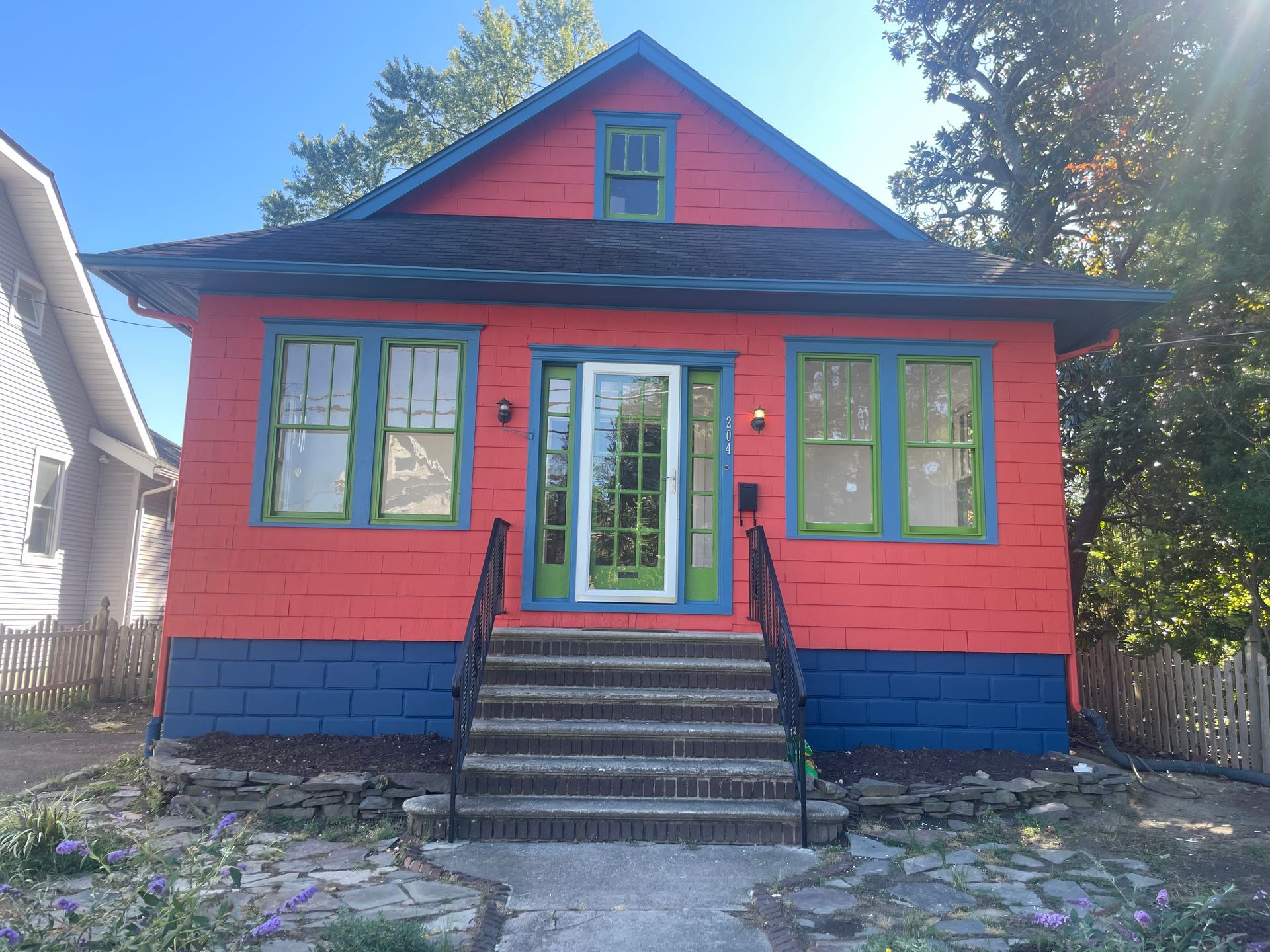 Brightly painted house with red walls, blue foundation, green trim, and a small porch.