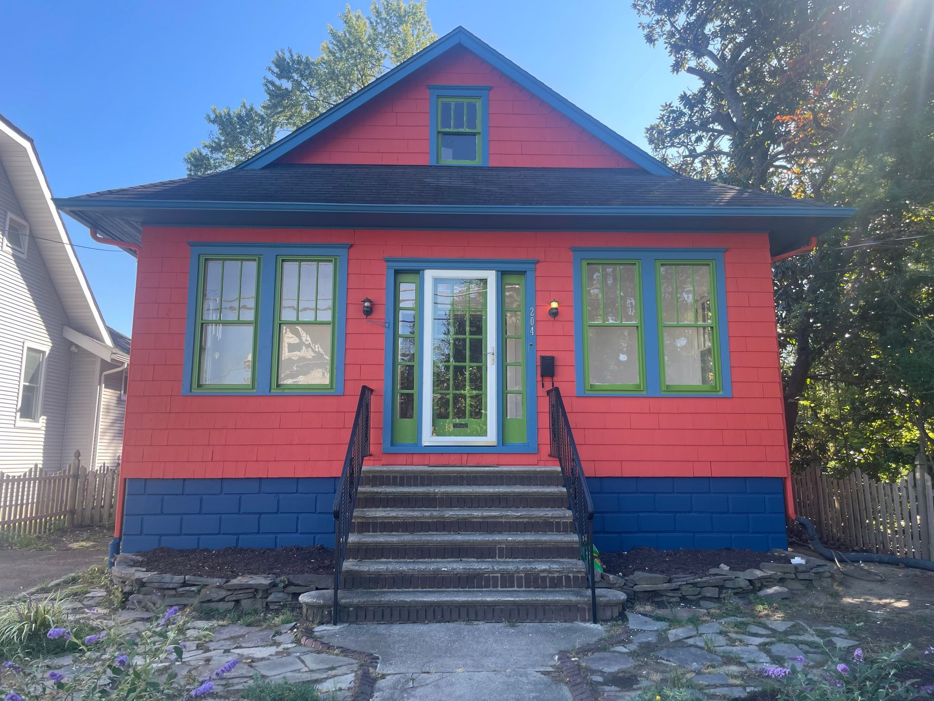 Brightly painted house with red upper and blue lower levels, green trim, and a centered glass door with steps leading up.