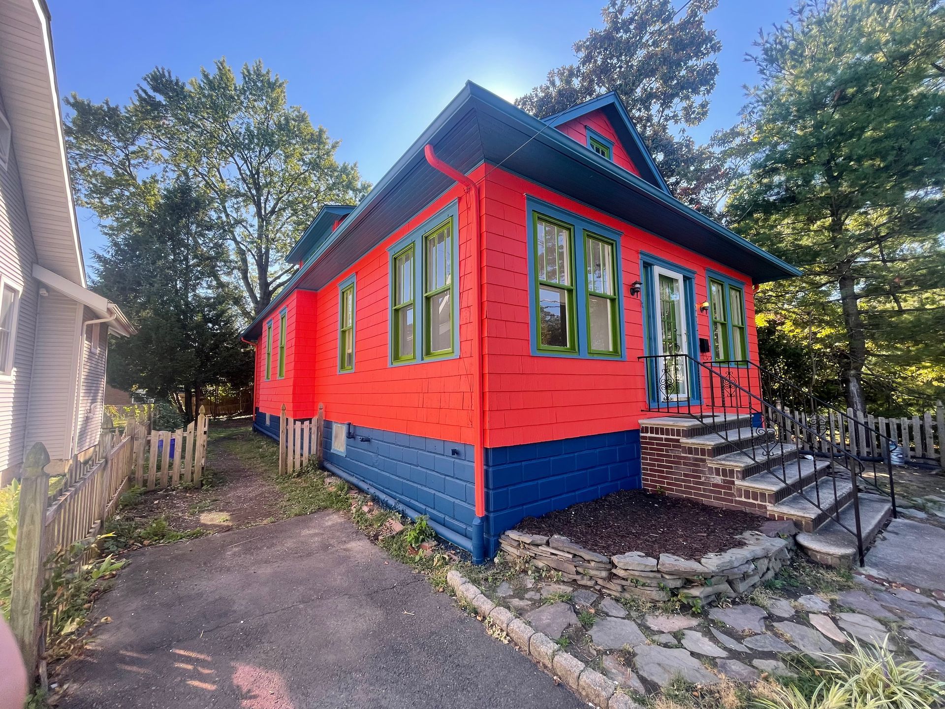 Red and blue house with green trim, set in a yard with a stone walkway and a small fence.