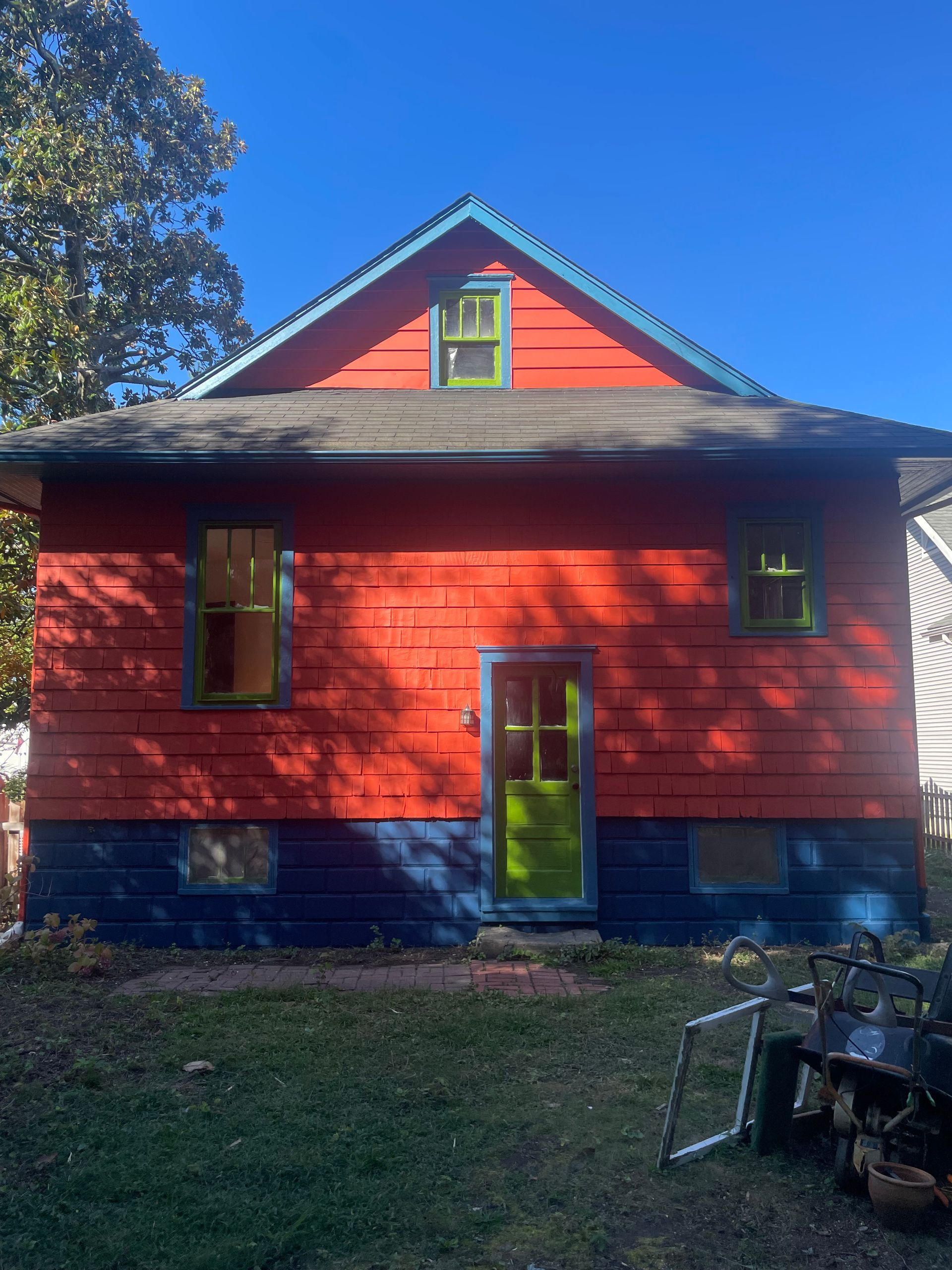 Red house with green trim and blue accents against a clear blue sky.
