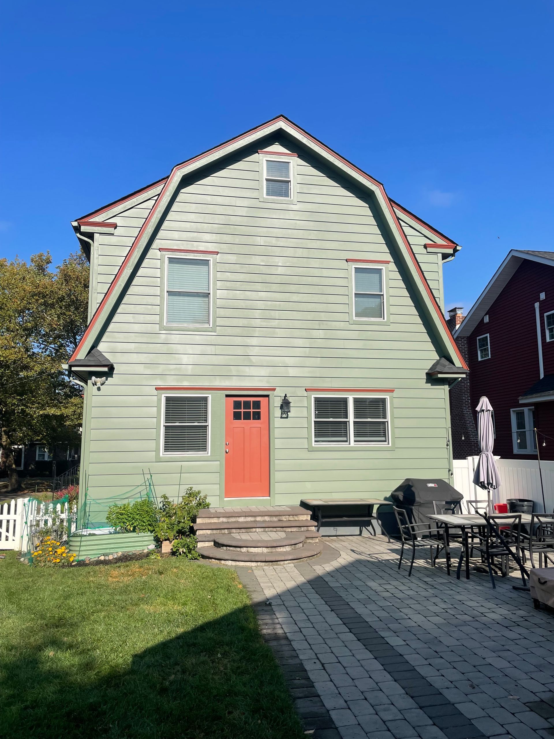 Green house with red door and trim, blue sky. Backyard patio with furniture.