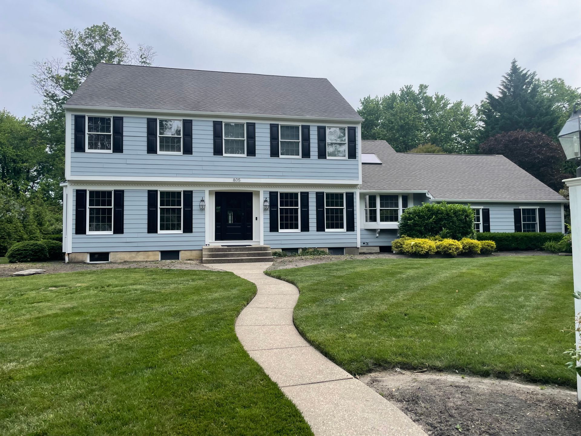 Light blue two-story house with black shutters, a winding walkway, and green lawn.