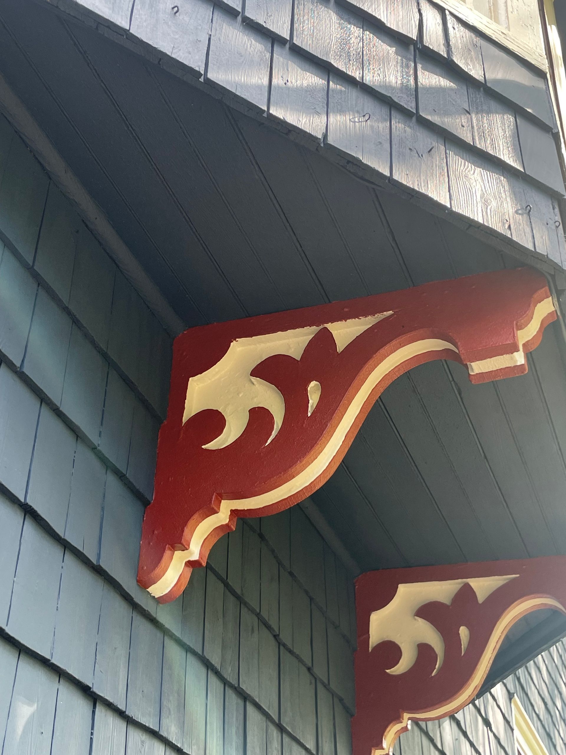 Red and cream decorative brackets on a blue-shingled building's overhang.